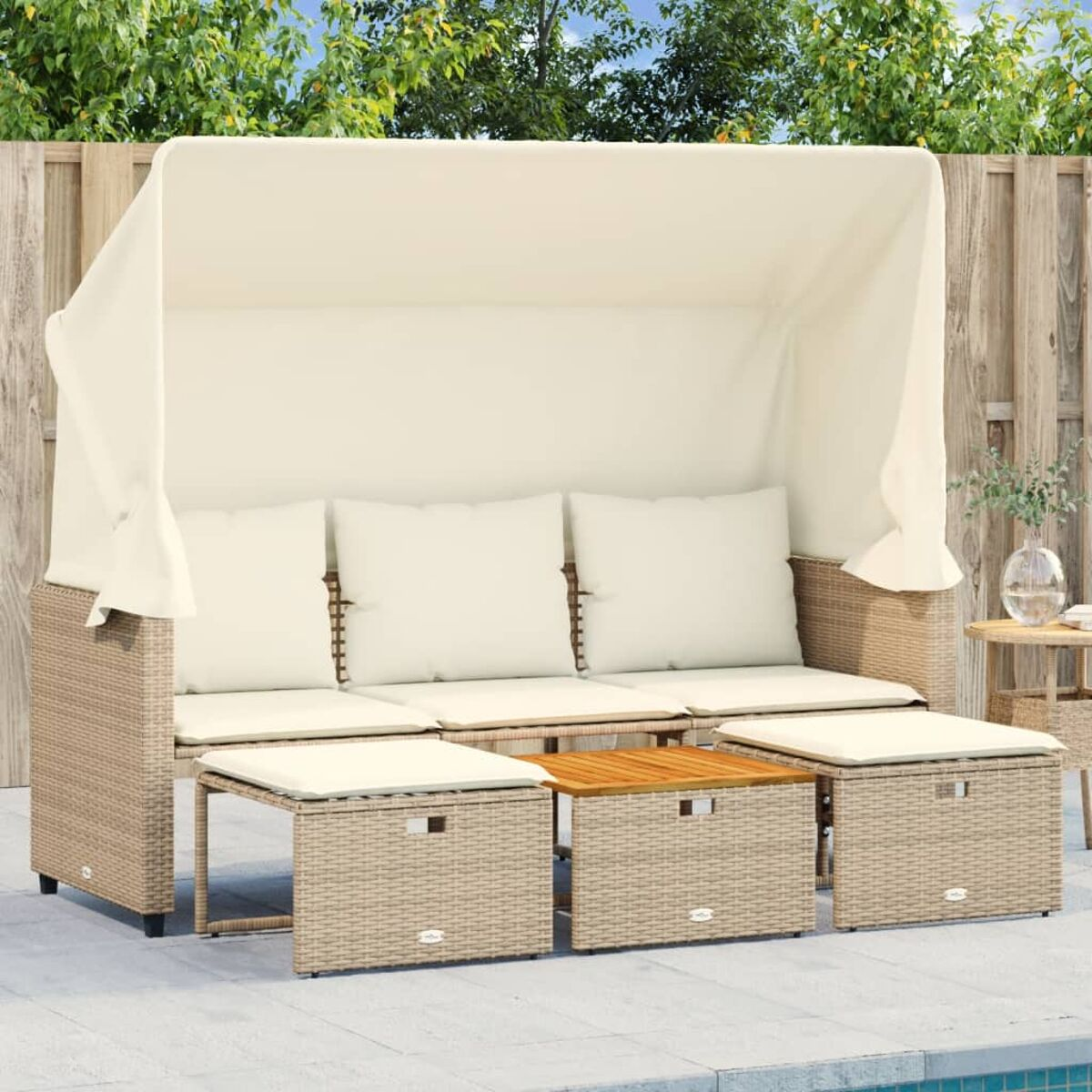 Sedute all'aperto con tenda. Cuscini beige, tre sgabelli e un tavolo in legno. Giorno di sole.