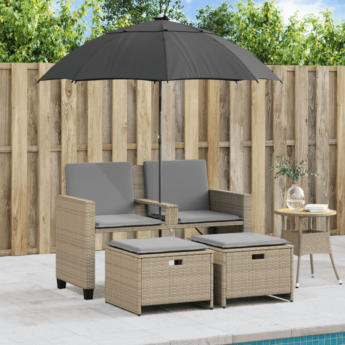 Set di sedute in vimini per esterni con ombrellone nero, cuscini grigi e tavolino a bordo piscina.