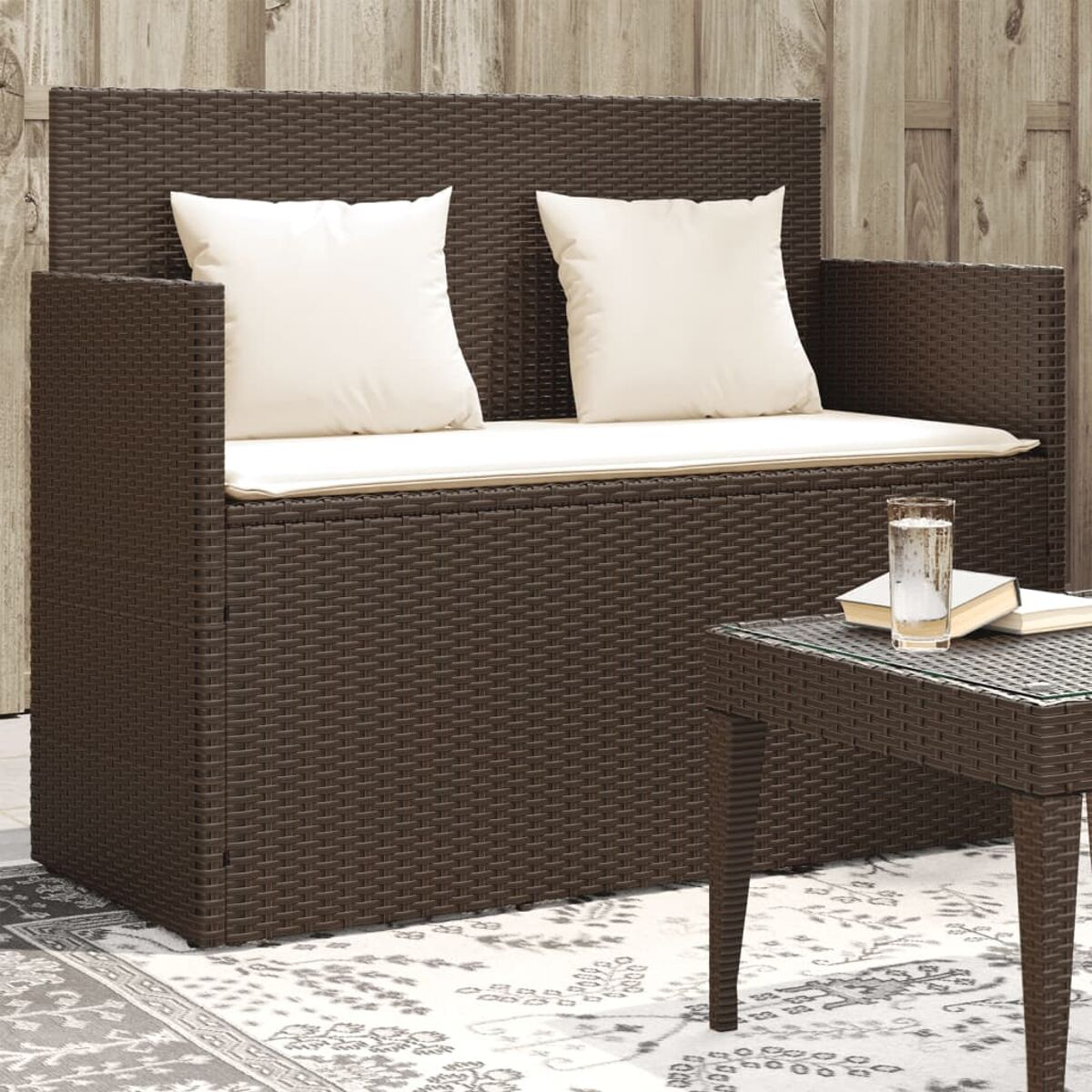 Braunes Outdoor-Sitzmöbelset aus Korbgeflecht mit Kissen und einem kleinen Tisch mit Glasplatte. Sonniger Tag.