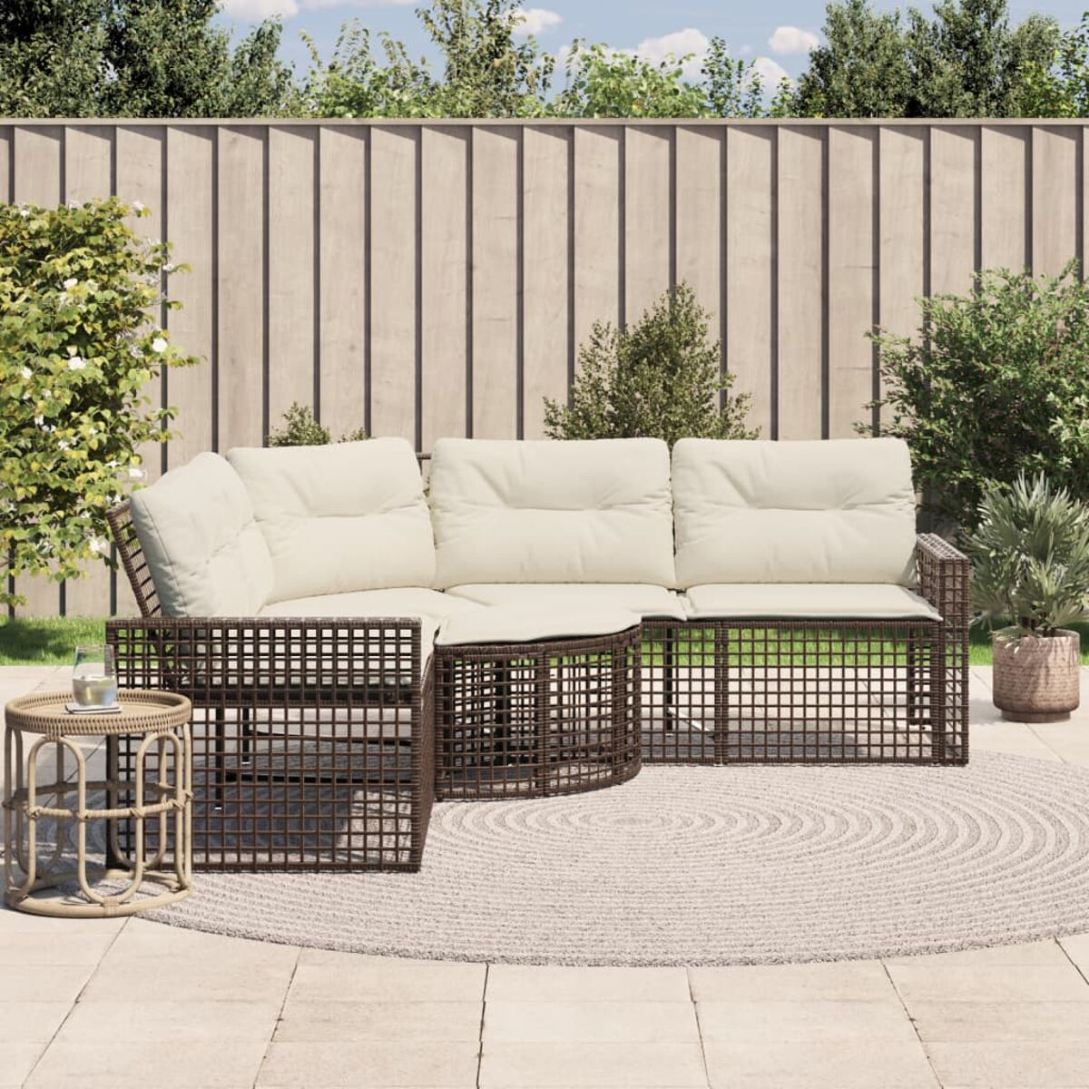 Braunes Outdoor-Ecksofa aus Korbgeflecht mit weißen Kissen auf einer Terrasse mit rundem Teppich und kleinem Tisch.