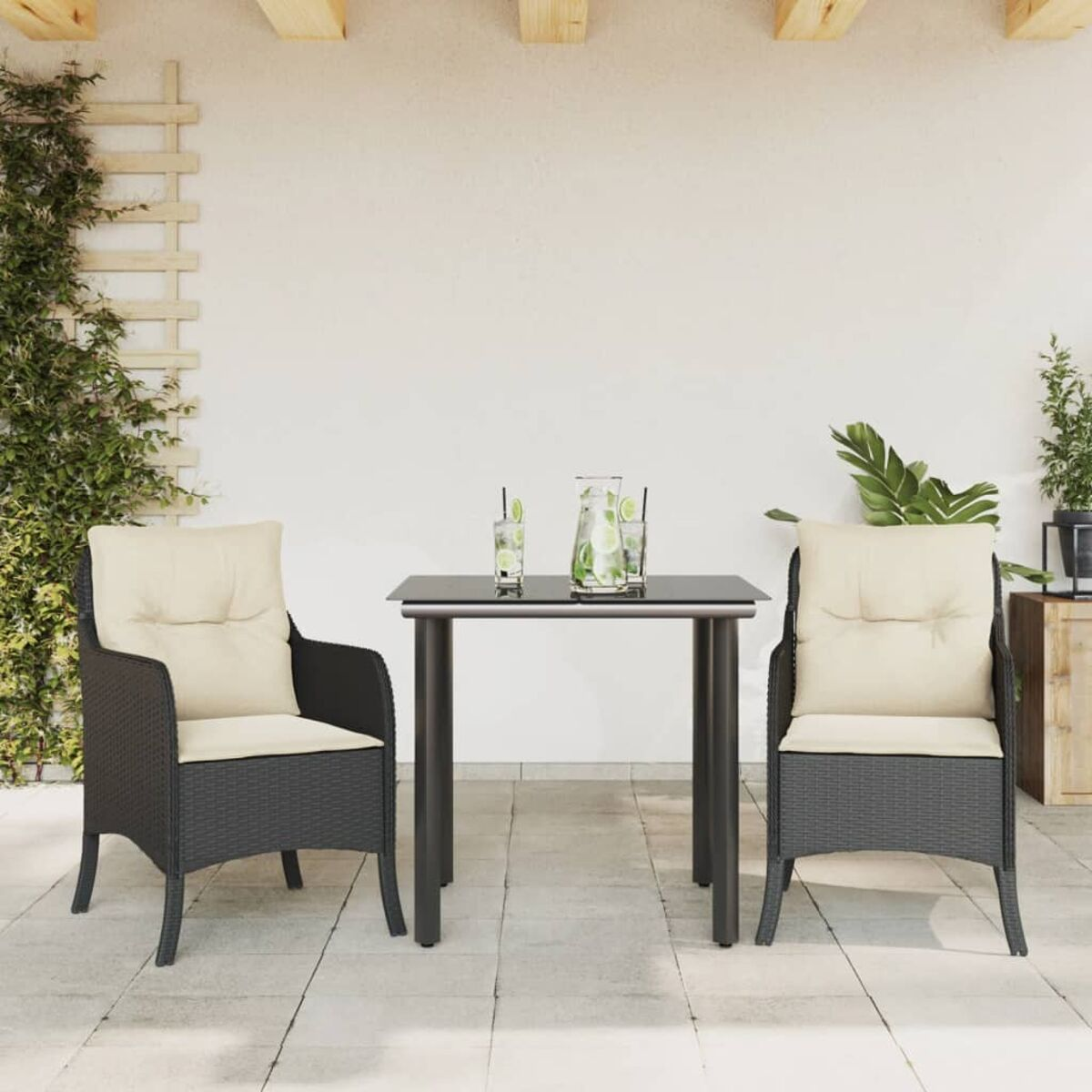 Essgruppe im Freien: zwei schwarze Korbstühle mit beigen Kissen, Tisch, weißer Wandhintergrund.