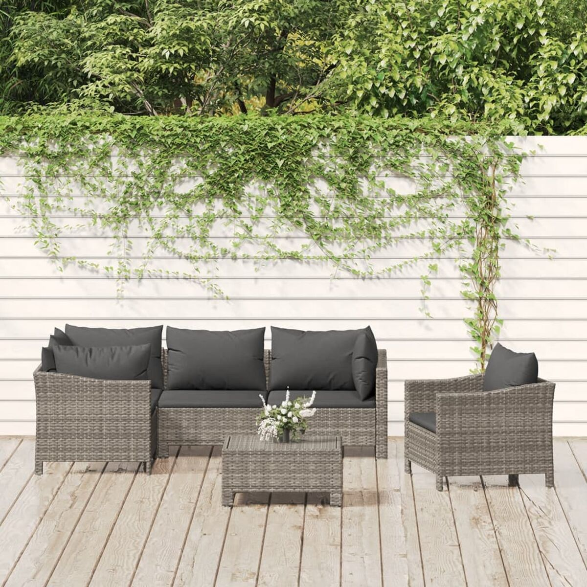 Terrassenmöbel mit Sofa, Sessel, Couchtisch und üppigem Grün.