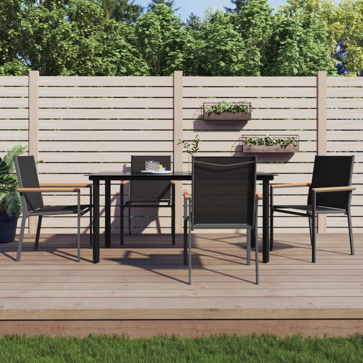 Essgruppe im Freien mit schwarzem Tisch und Stühlen auf einer Holzterrasse, grünem Gras und Holzzaun.