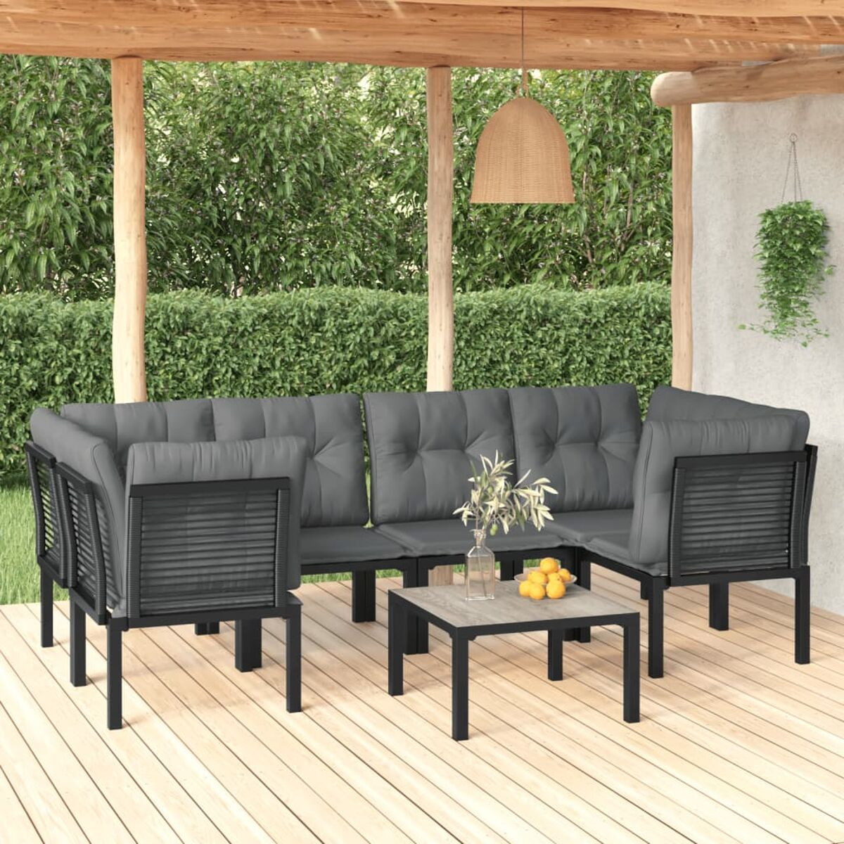 Graues Outdoor-Sofaset mit Kissen und einem kleinen Tisch auf einer Holzterrasse, mit grünem Hintergrund.