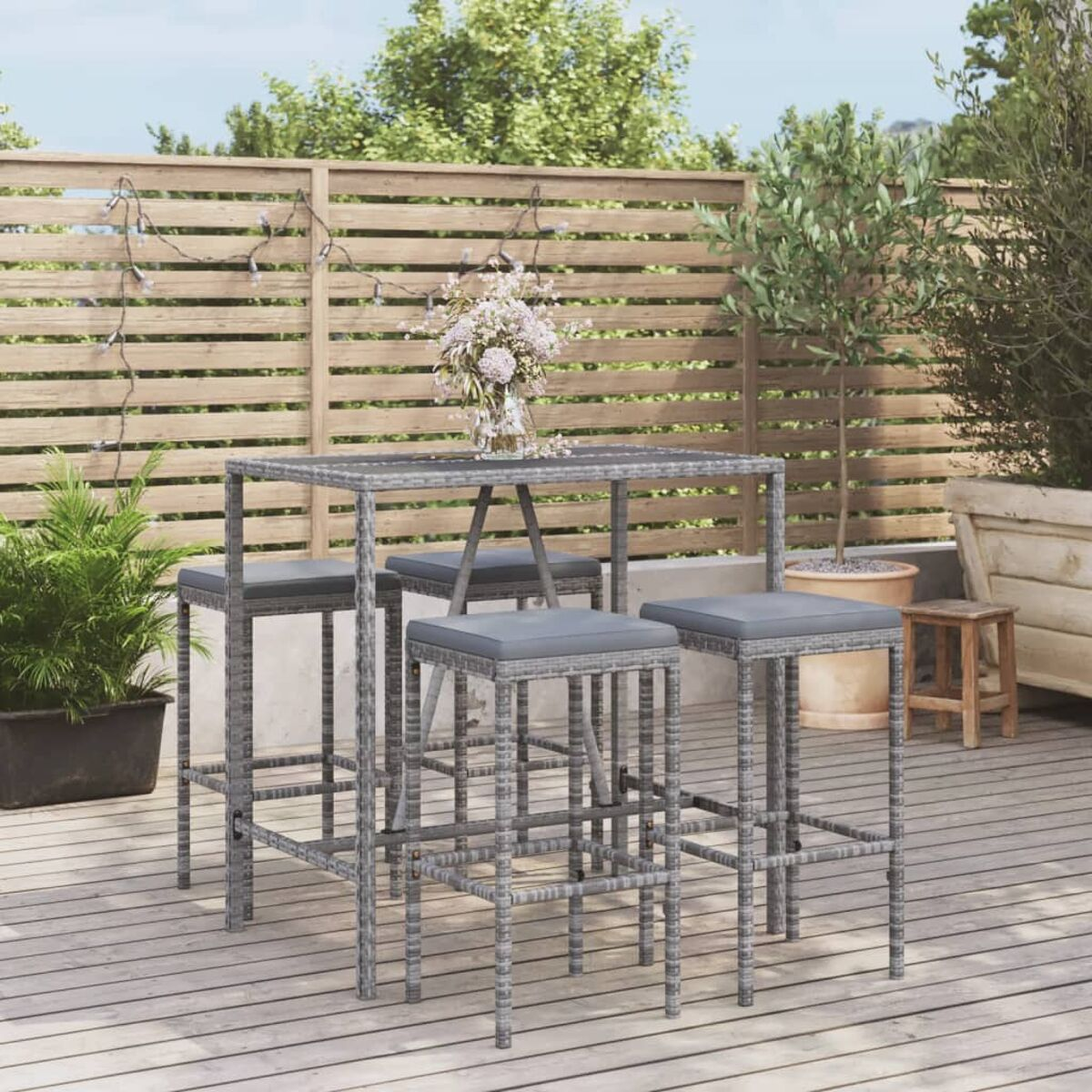 Essgruppe im Freien mit Tisch und Hockern. Der Tisch hat eine Glasplatte. Holzterrasse im Hintergrund.