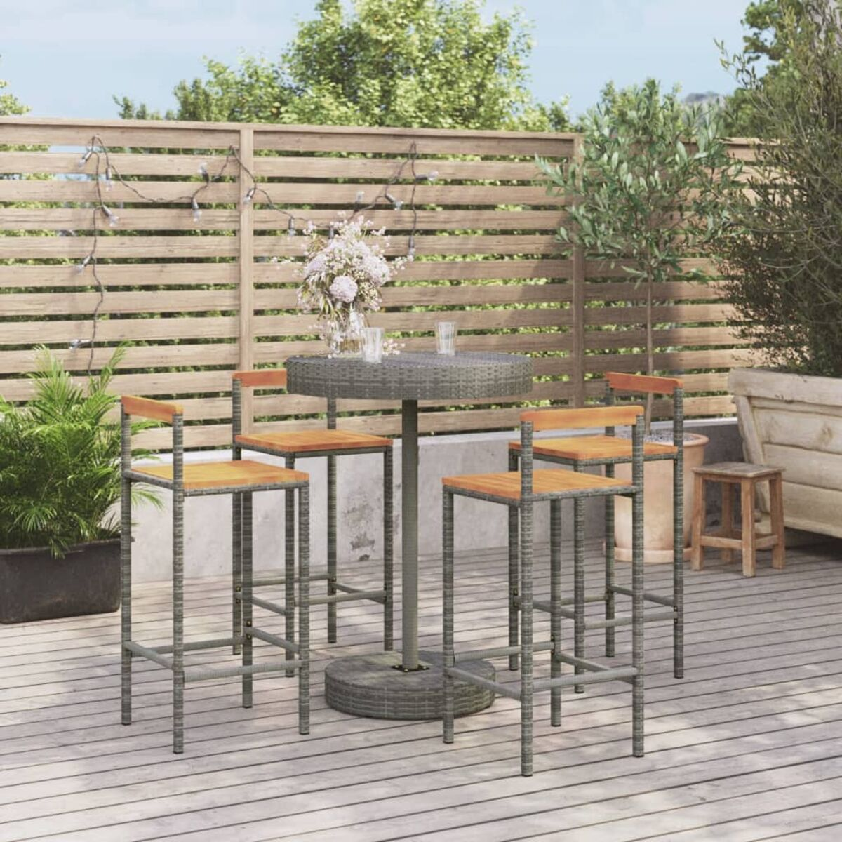 Outdoor-Bar-Set: runder Tisch, vier Hocker. Graues Korbgeflecht, Holzsitze. Blumen auf dem Tisch, Holzzaun.
