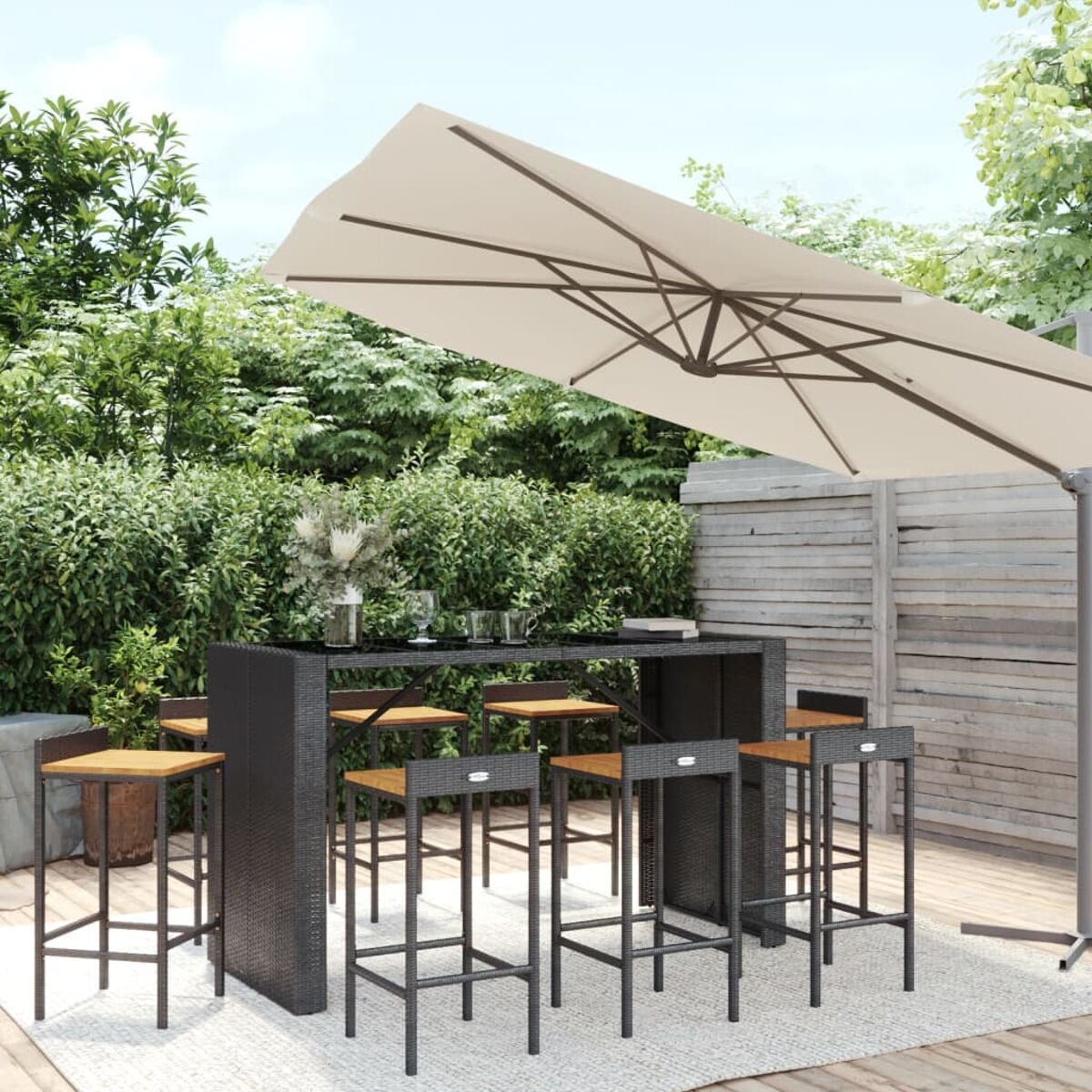 Eine Outdoor-Bar mit Hockern und einem großen Sonnenschirm. Grünes Laub und ein Holzzaun dahinter.