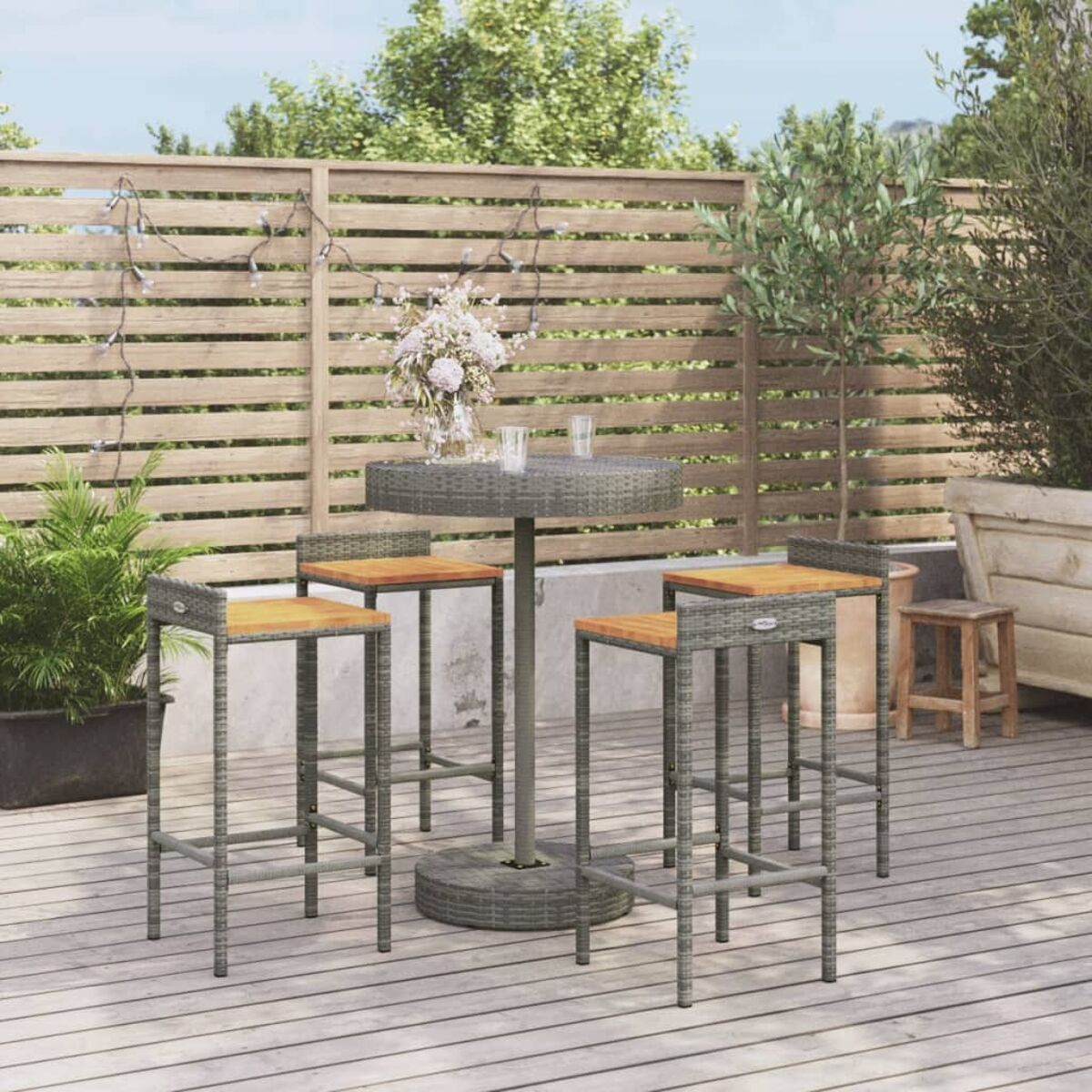 Outdoor-Setting mit rundem Tisch, vier Hockern und Pflanzen auf einem Holzdeck.