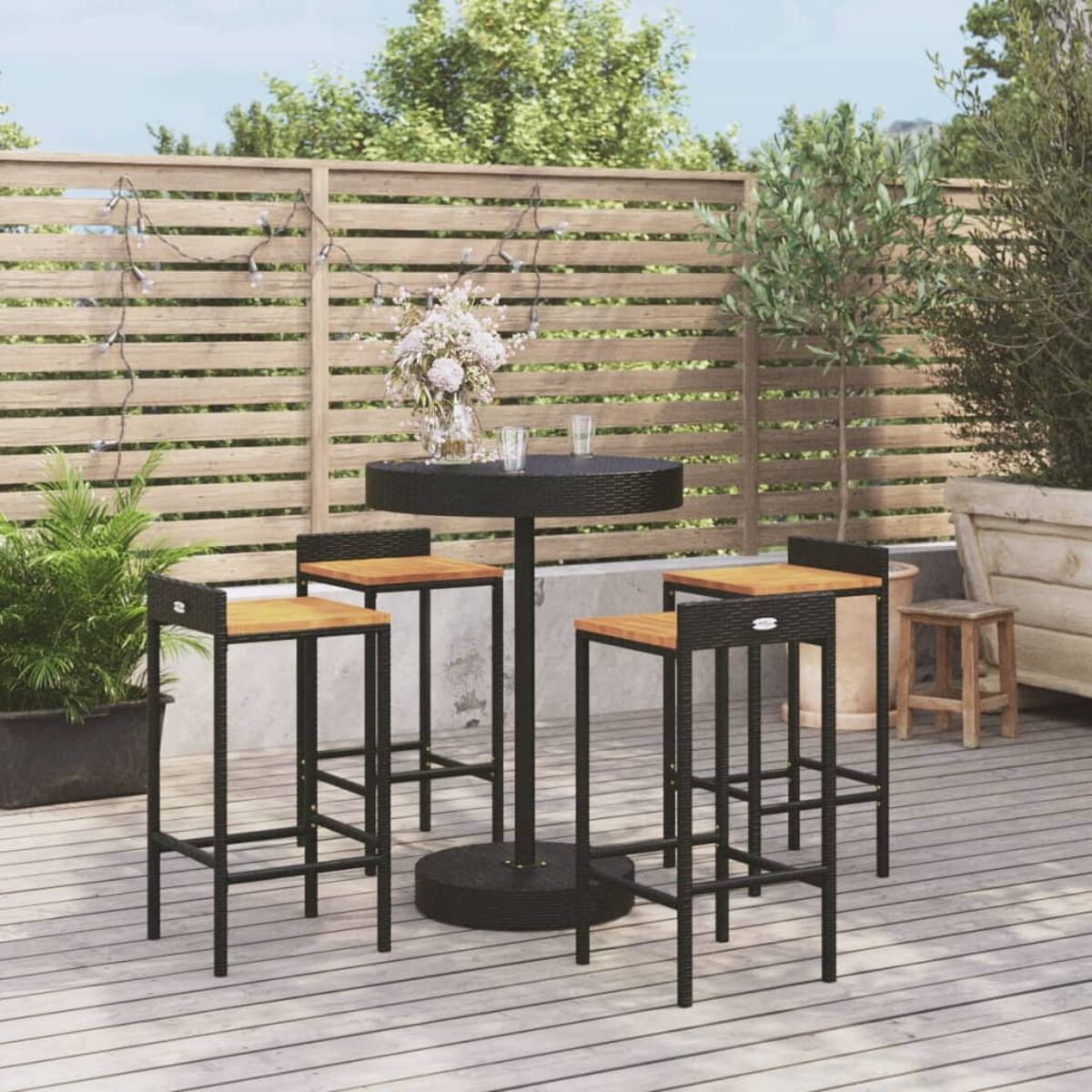 Ein runder Tisch mit Barhockern auf einem Holzdeck. Blumen und Pflanzen befinden sich auf dem Deck.
