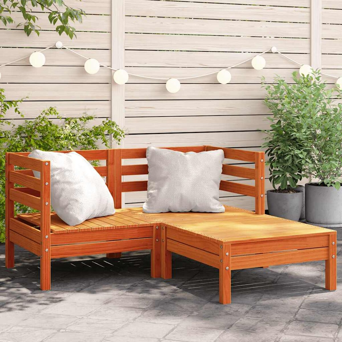 Holz-Ecksofa und kleiner Tisch auf einer Terrasse. Grüne Pflanzen und Holzzaun im Hintergrund.