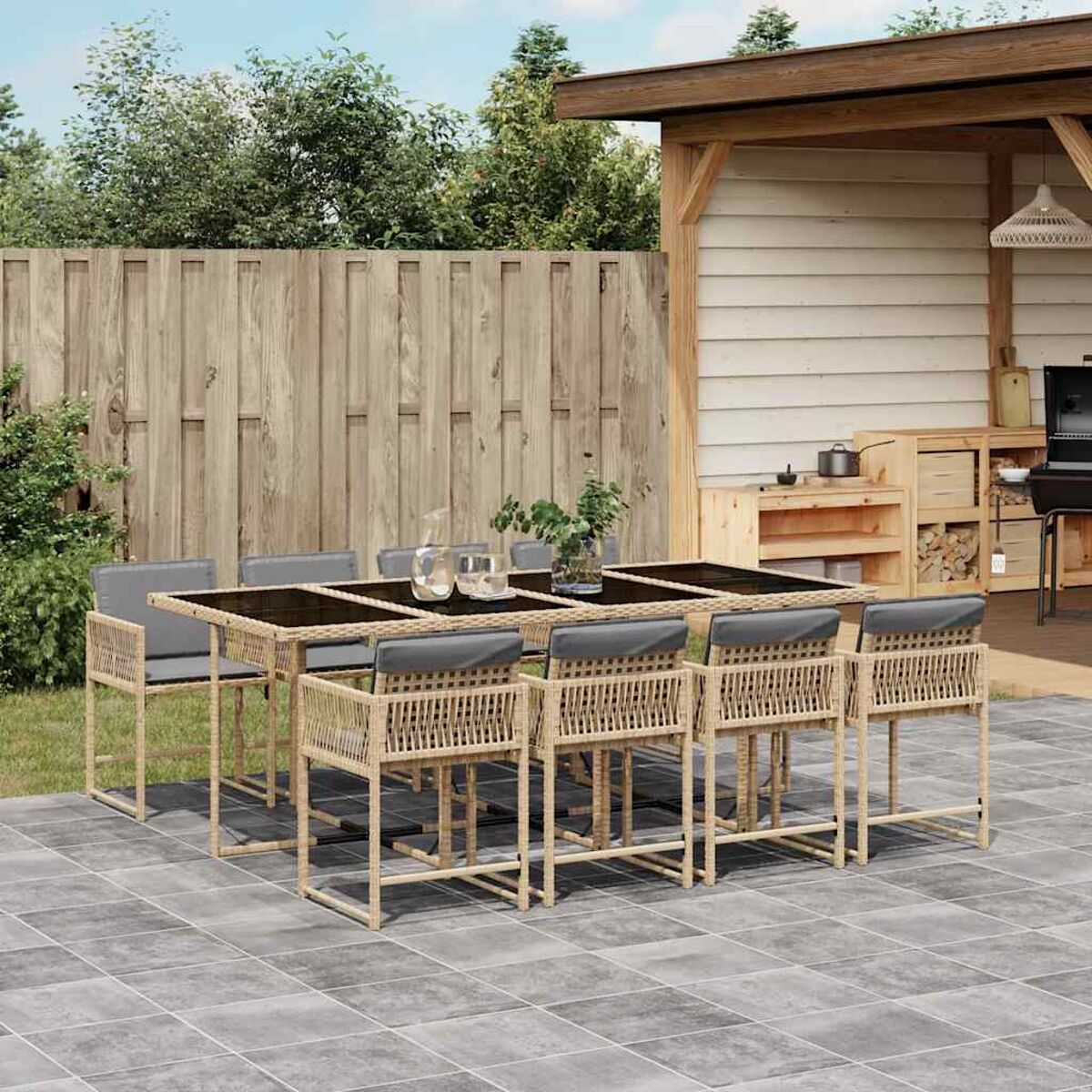 Set da pranzo all'aperto con tavolo nero e sedie in vimini beige. Recinzione in legno sullo sfondo.