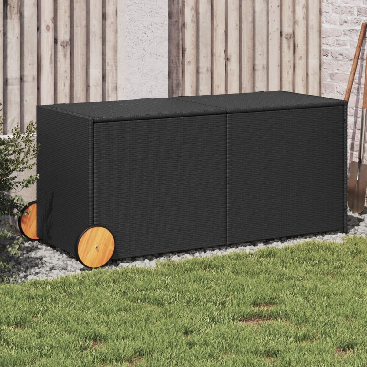 Schwarze Aufbewahrungsbox aus Korbgeflecht mit Holzrädern. Auf Gras und Stein platziert.