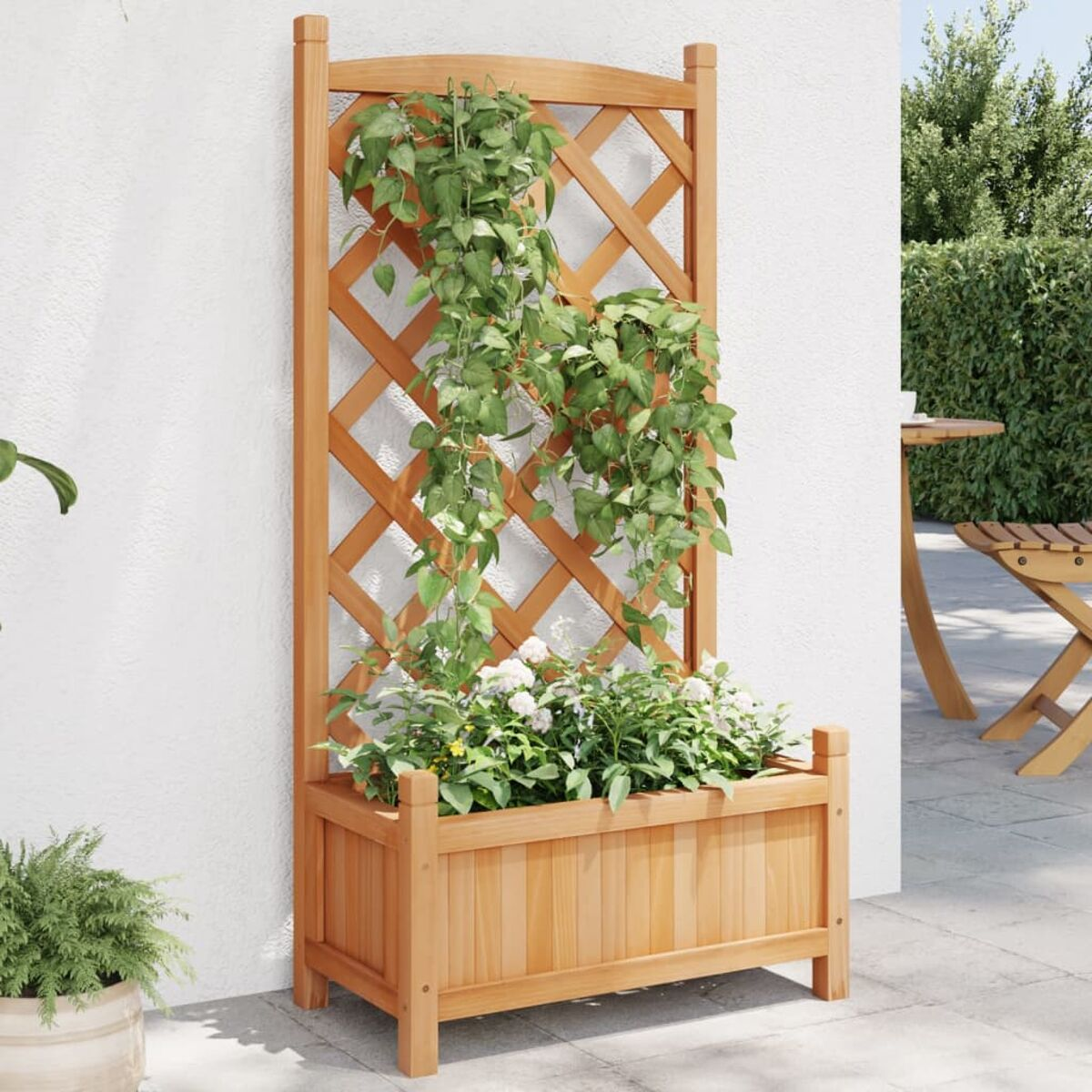 Holzgitter mit Pflanzen. Unterhalb befindet sich ein Pflanzkasten, im Hintergrund eine Wand und eine Terrasse.