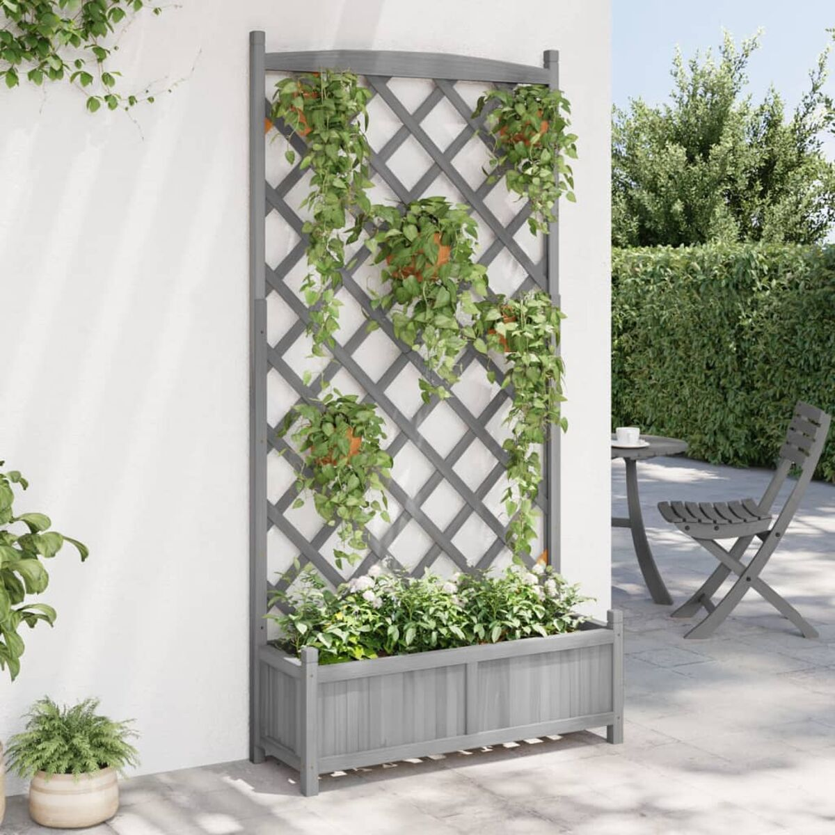 Ein graues Spalier mit Pflanzen und Blumen. Es hat einen hölzernen Pflanzkasten an der Basis.