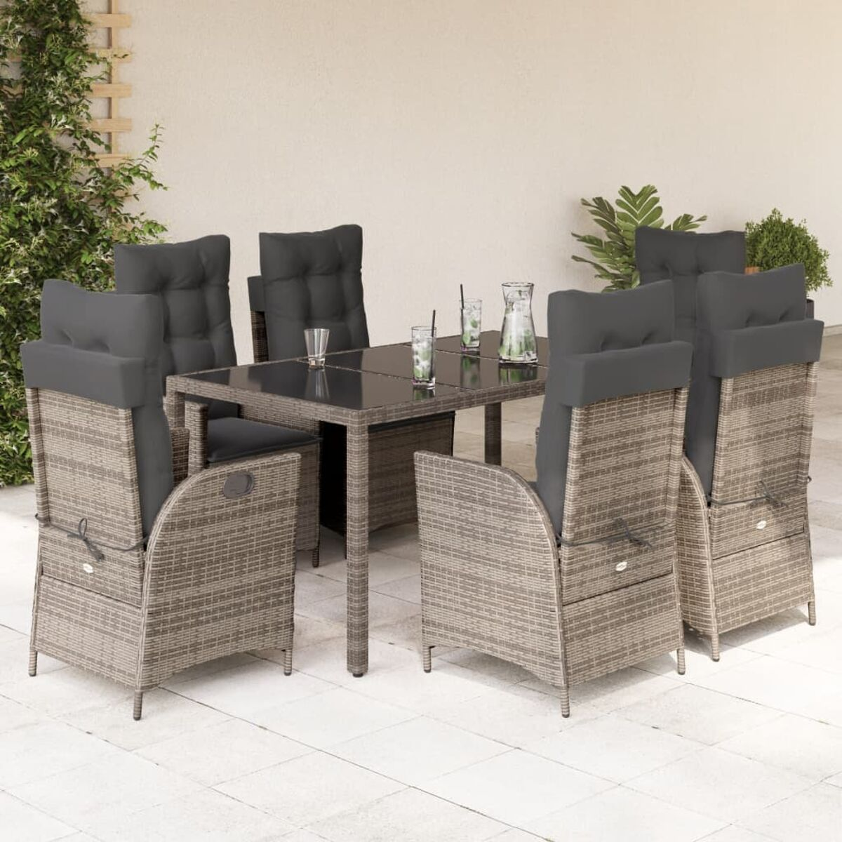 Set da pranzo all'aperto. Sedie in rattan con cuscini grigi attorno a un tavolo di vetro.