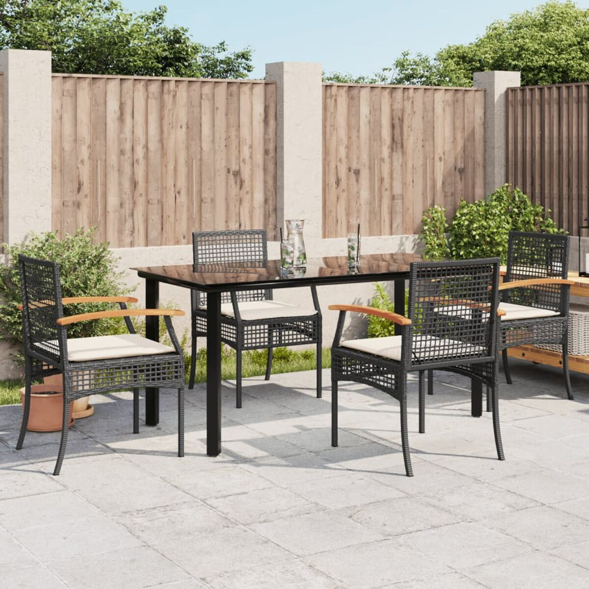 Essgruppe für draußen: dunkle Stühle, Tisch mit Glasplatte, Terrasse, Garten im Hintergrund.