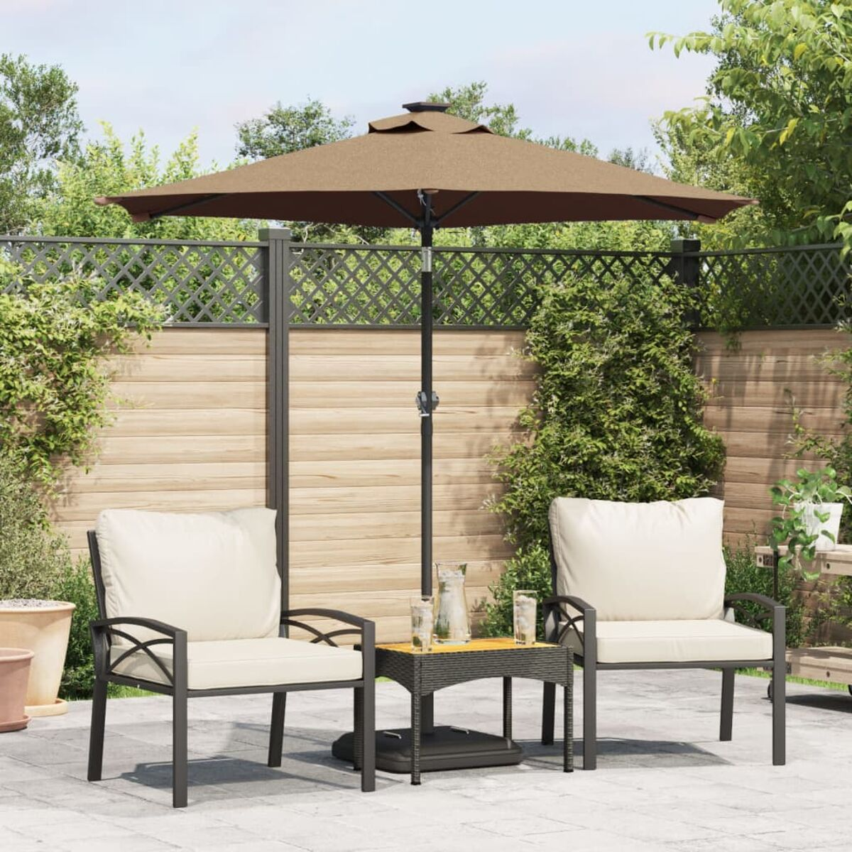 Terrassenmöbel-Set mit zwei Stühlen, Sonnenschirm und kleinem Tisch. Dunkle Stühle mit cremefarbenen Kissen.