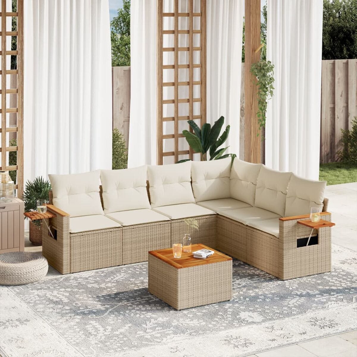 Geflochtenes Outdoor-Ecksofa mit cremefarbenen Kissen und einem Tisch. Weiße Vorhänge im Hintergrund.