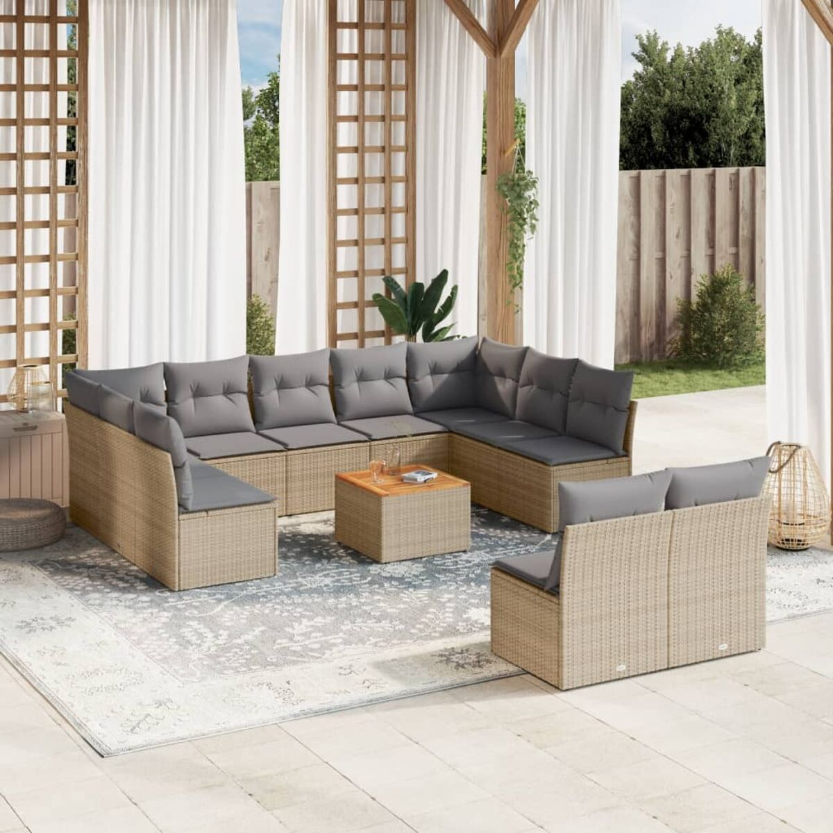 Beiges Rattan-Outdoor-Ecksofa mit grauen Kissen, quadratischer Tisch. Weiße Vorhänge und ein Teppich vervollständigen die Szene.