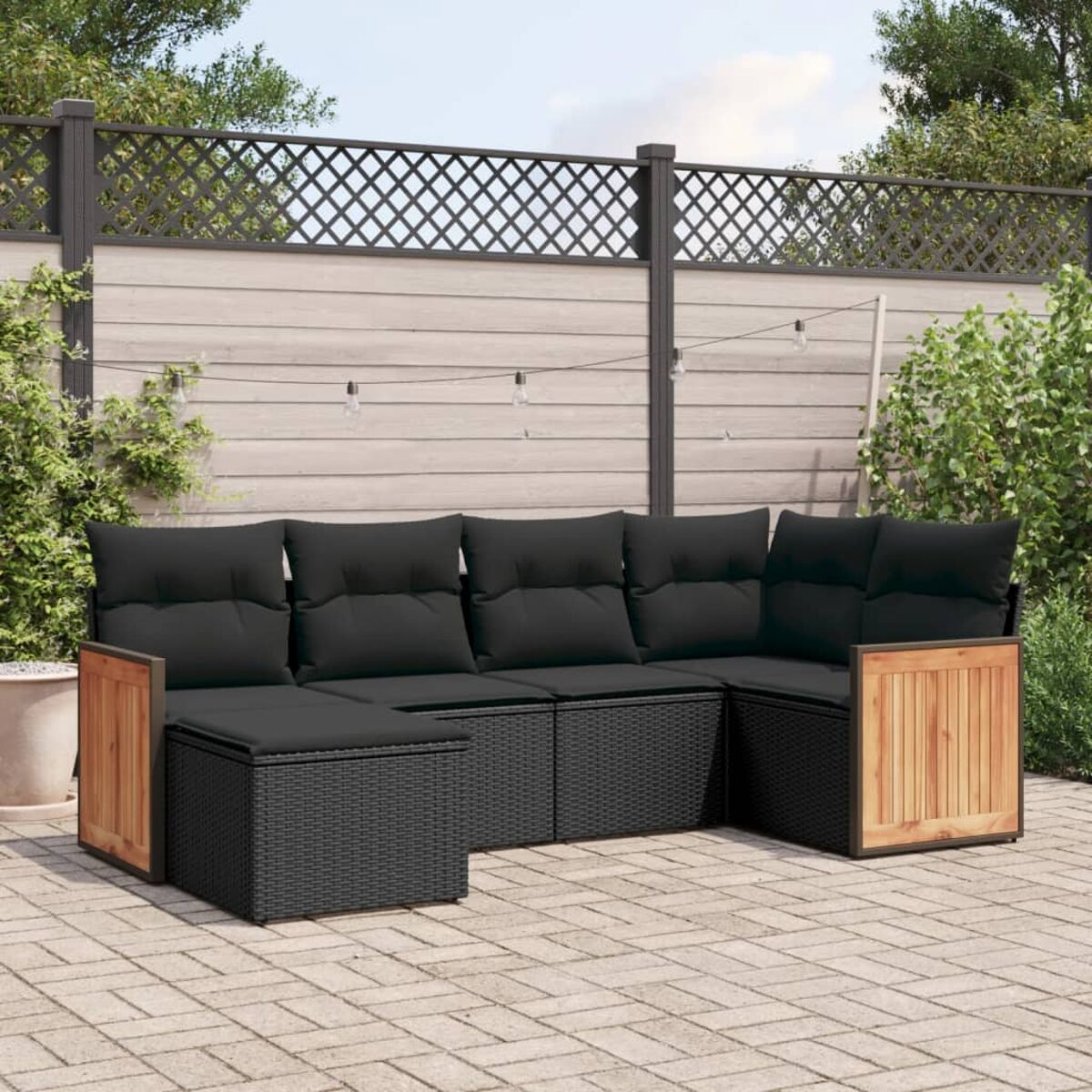 Schwarzer Rattan-Outdoor-Schnitt mit Holzakzenten. Schwarze Kissen auf Ziegelpflaster im Garten. Holzzaun im Hintergrund.