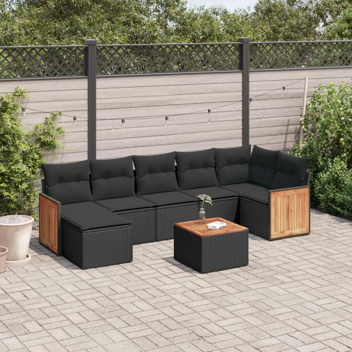 Outdoor-Möbelset aus schwarzem Korbgeflecht mit Kissen, Tisch und Gartenhintergrund.
