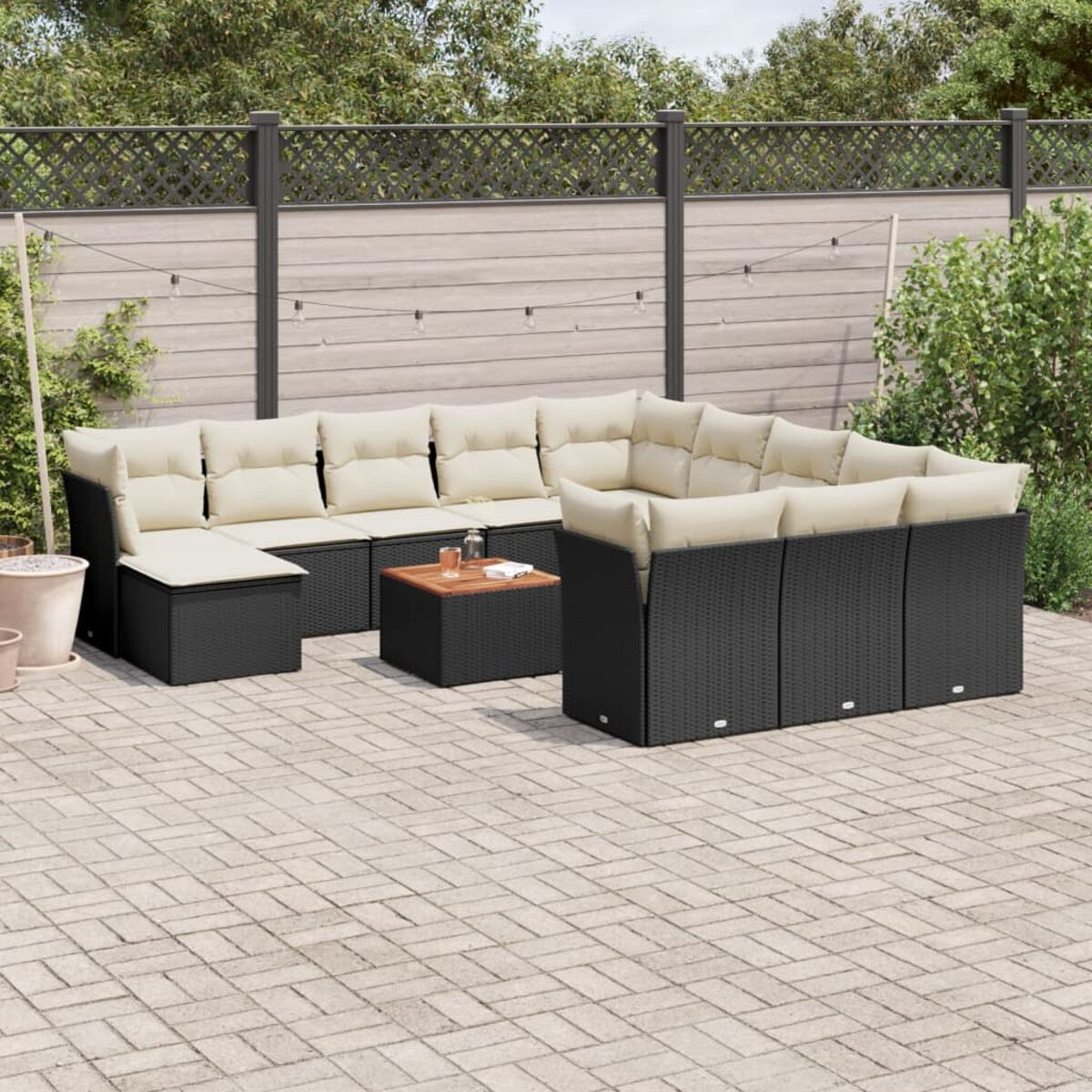 Schwarzes Rattan-Terrassenset mit beigen Kissen, quadratischem Tisch. Pflastersteine im Hintergrund.