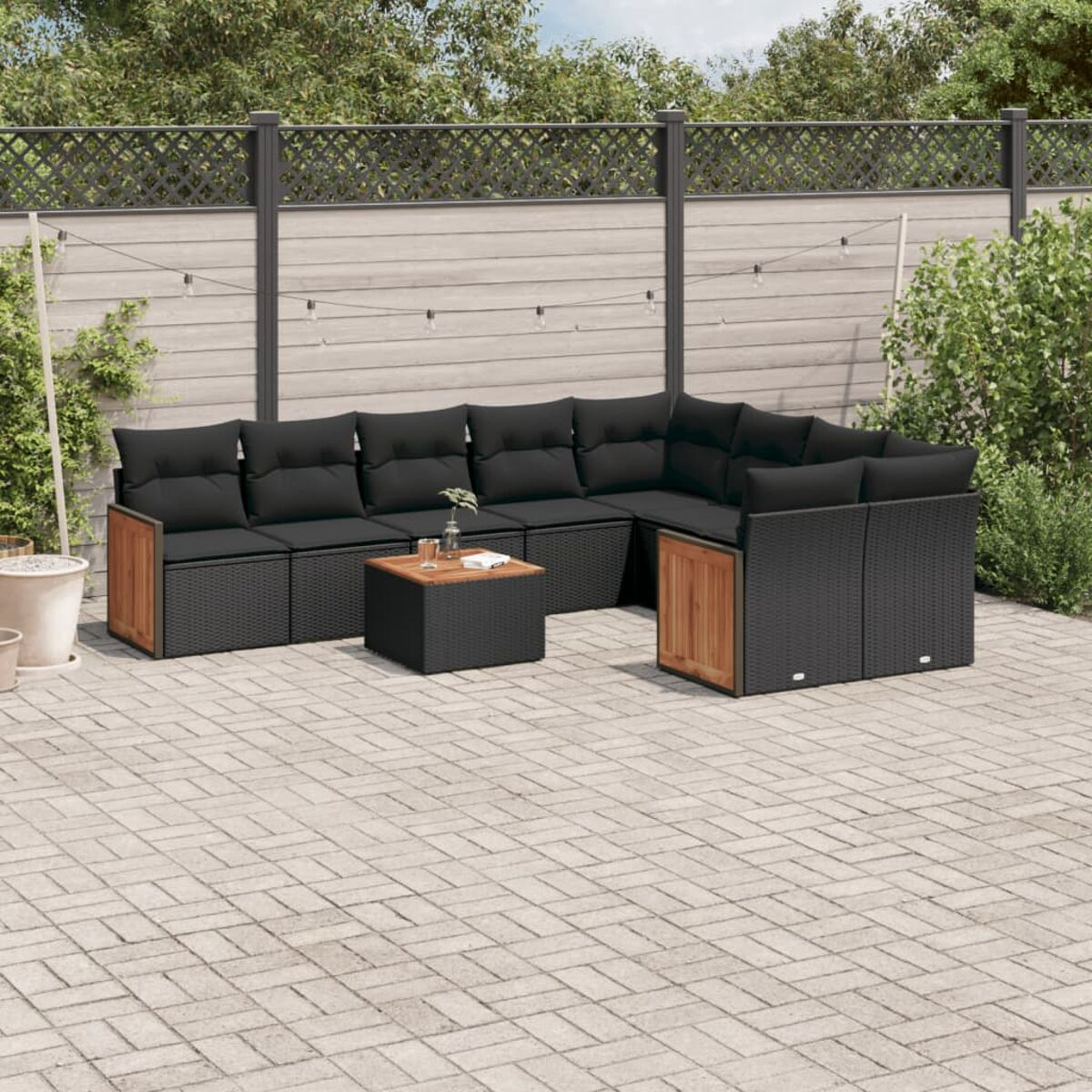 Outdoor-Ecksofa mit schwarzen Kissen, einem Holztisch und einer grauen Backstein-Terrasse mit Zaun.