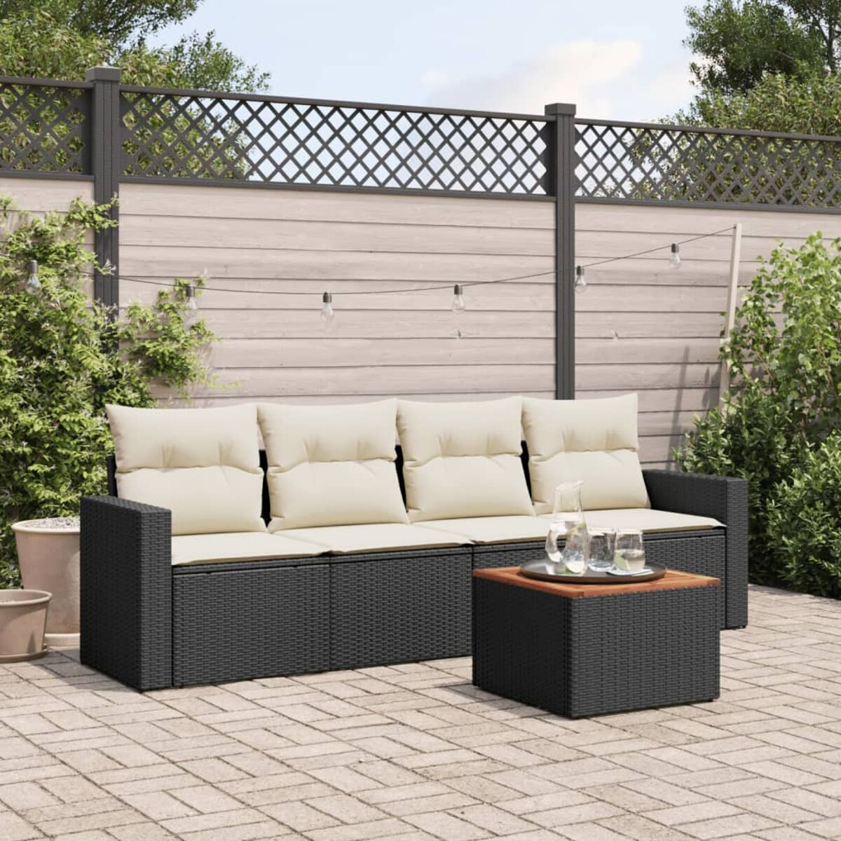 Schwarzes Rattan-Sofa und quadratischer Tisch. Beige Kissen. Ziegelterrasse. Grün.