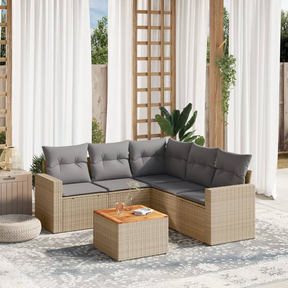 Ecksofa aus Korbgeflecht mit grauen Kissen. Holztisch und weiße Vorhänge. Hellfarbiger Teppich auf der Terrasse.