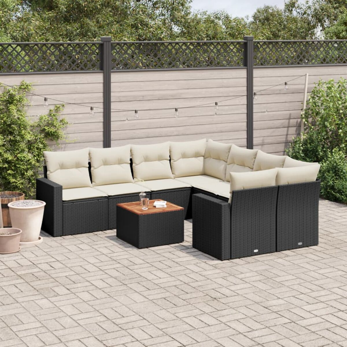 Wohnzimmer-Set für draußen. Schwarze Rattanmöbel mit cremefarbenen Kissen. Steinboden, Holztisch.
