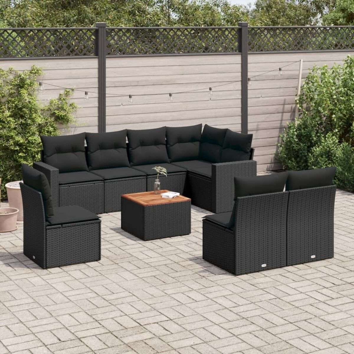 Outdoor-Ecksofa schwarz mit schwarzen Kissen und einem Couchtisch aus Holz. Grünes Laub im Hintergrund.