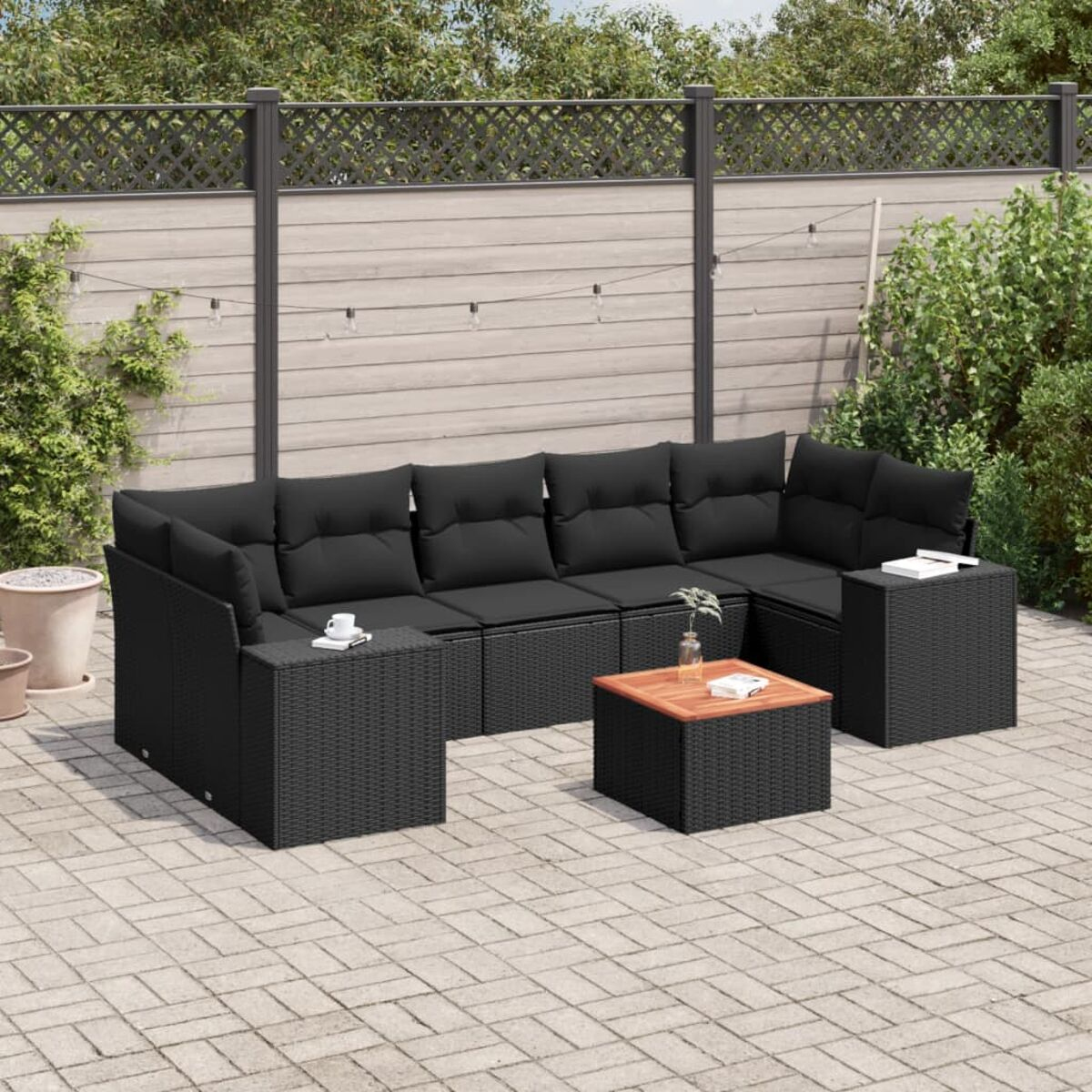 Schwarzes Korbmöbel-Gartensofa mit schwarzen Kissen, ein Holztisch. Gepflasterte Terrasse.