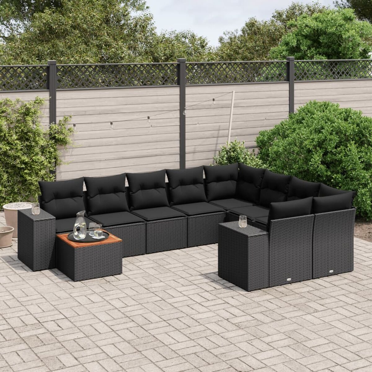 Sitzgruppe für den Außenbereich. Schwarze Rattanmöbel mit schwarzen Kissen. Gepflasterter Bereich.