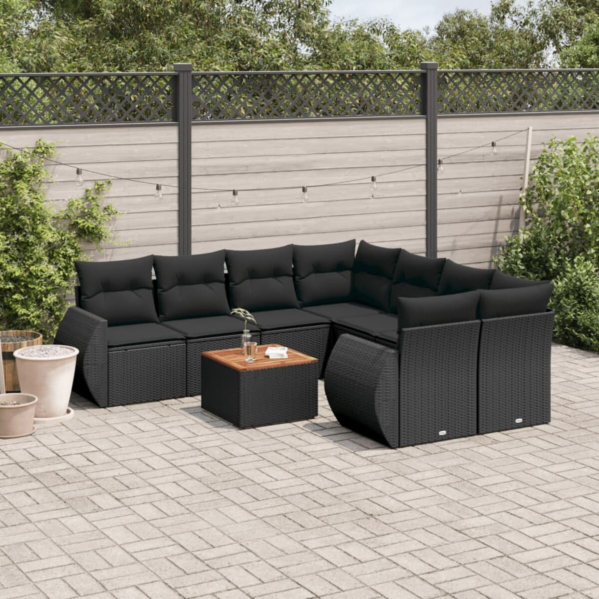 Schwarzes Ecksofa-Set aus Korbgeflecht mit schwarzen Kissen und Tisch. Auf einer Terrasse im Freien.