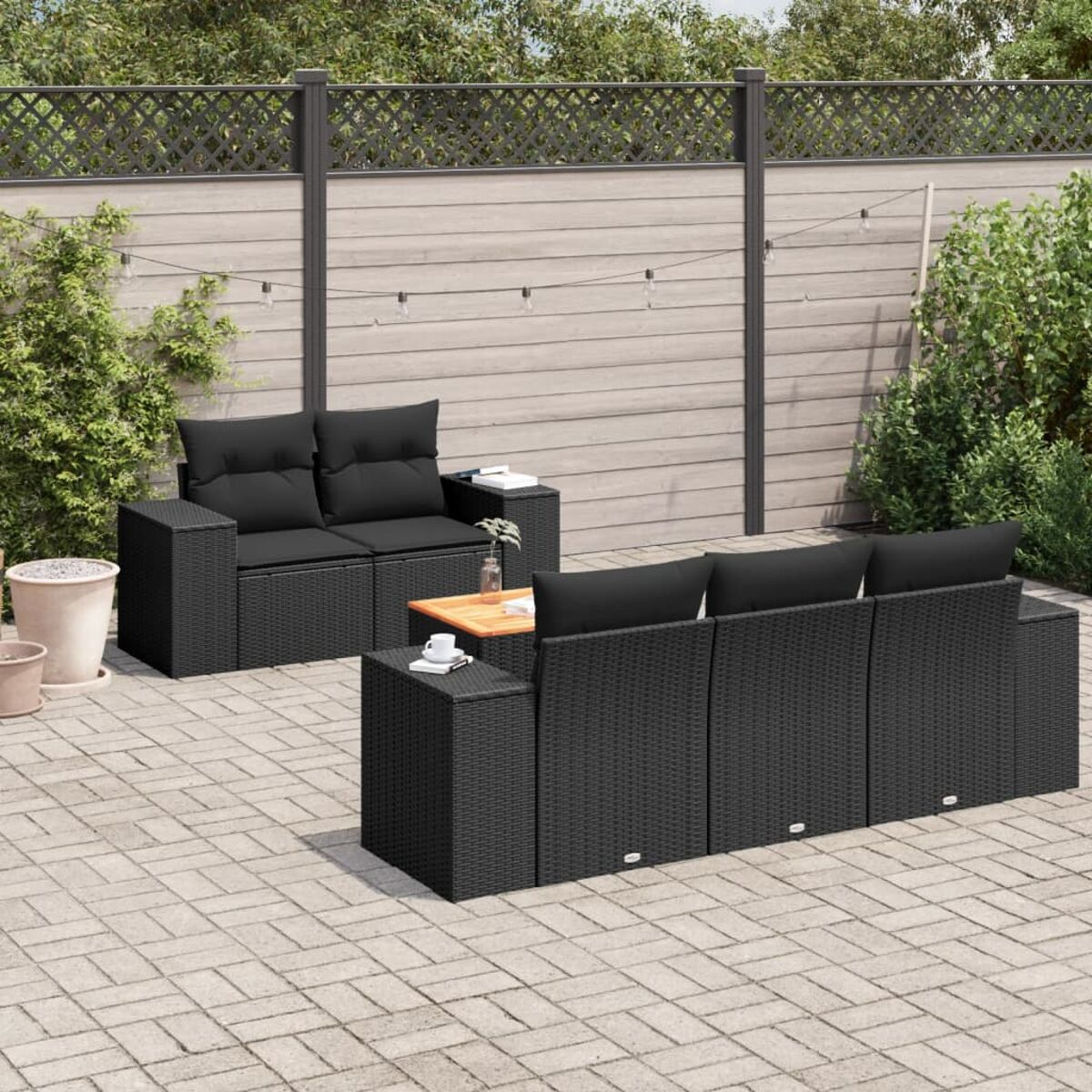 Sitzgruppe im Freien mit schwarzen Möbeln, schwarzen Kissen und einem Holztisch. Backstein-Patio, grüne Pflanzen.