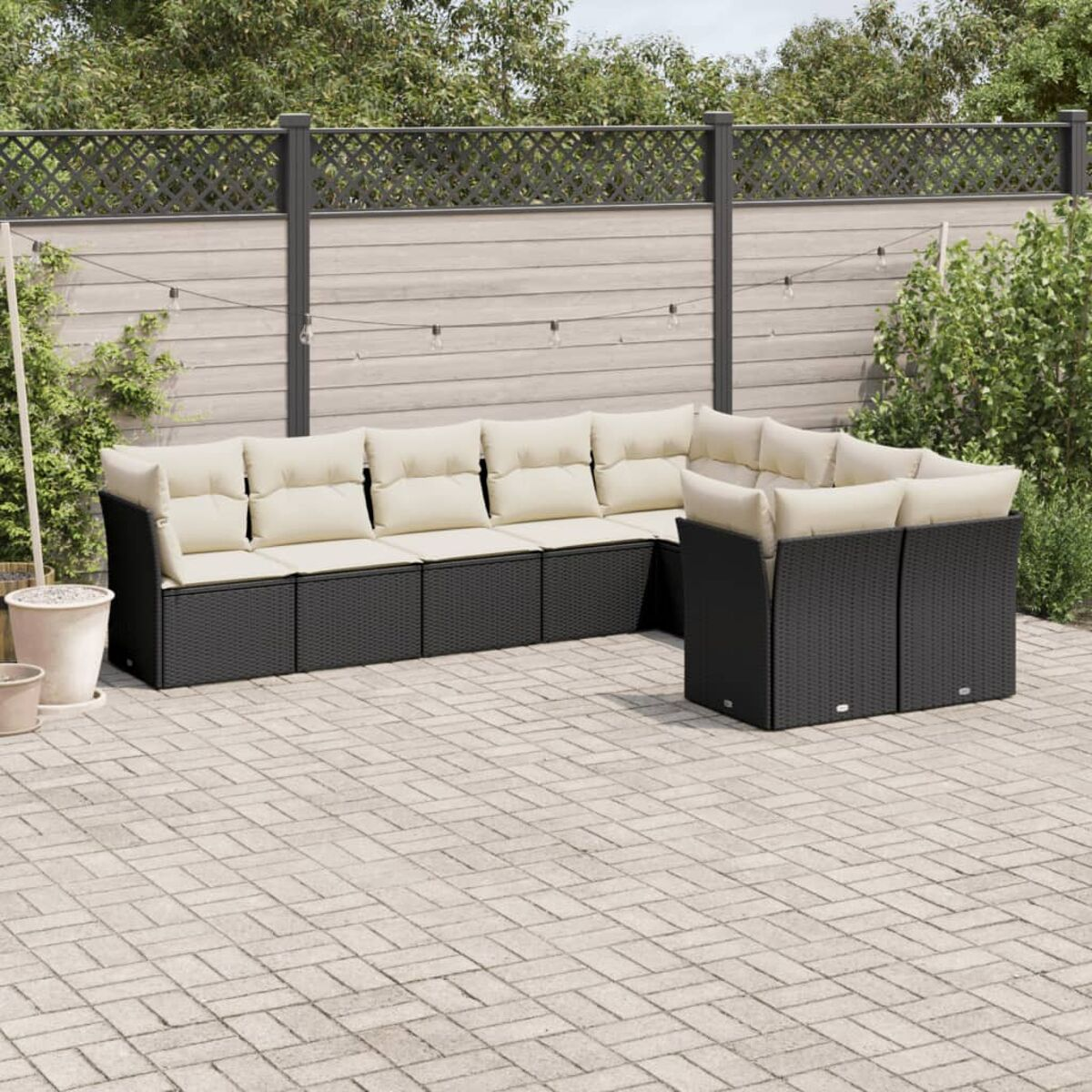 Outdoor-Ecksofa mit beigefarbenen Kissen, schwarzem Rahmen, auf Ziegelpflaster, mit grünem Laub.