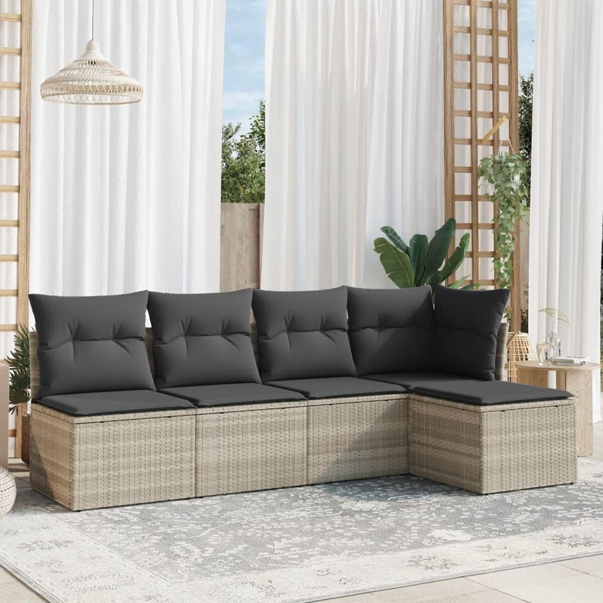 Ein Outdoor-Ecksofa aus Rattan mit grauen Kissen auf einer Terrasse mit Teppich und Vorhängen.
