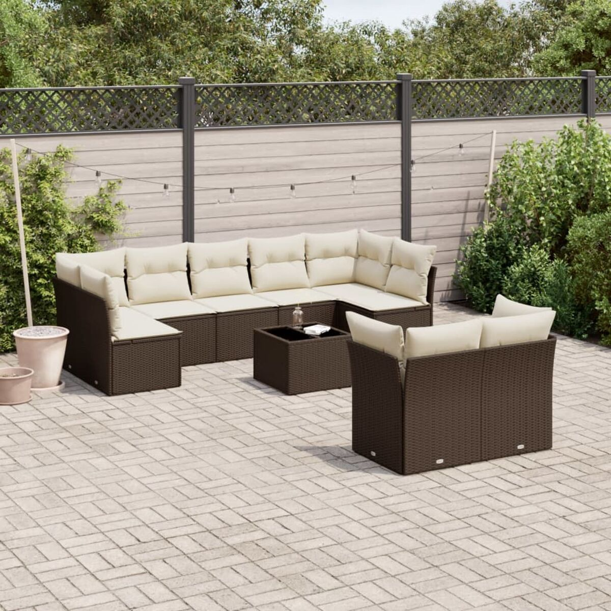 Divano componibile in vimini marrone con cuscini beige e tavolino quadrato, in giardino.