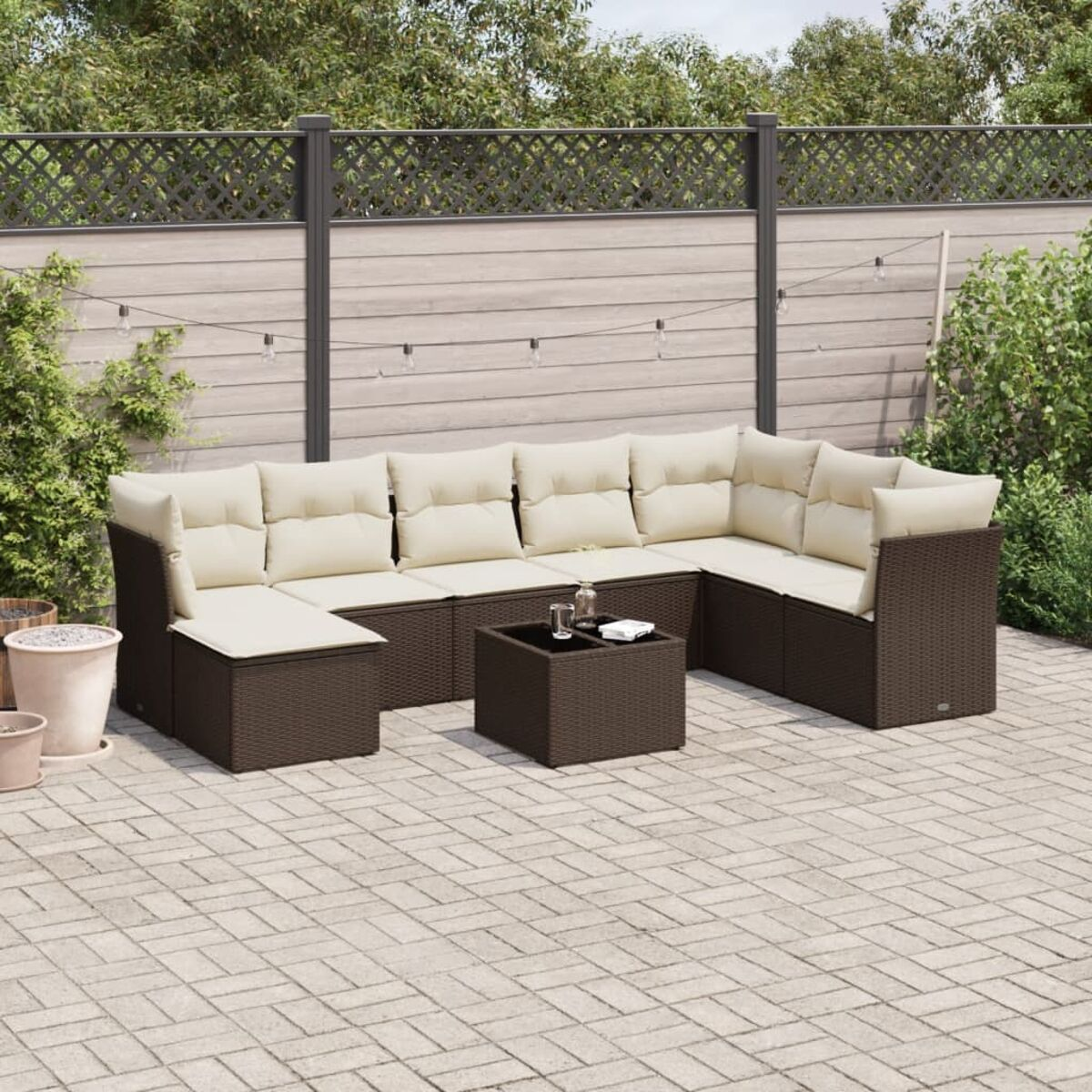 Set divano in rattan da esterno: marrone con cuscini beige, tavolo quadrato. Patio in mattoni, recinzione.