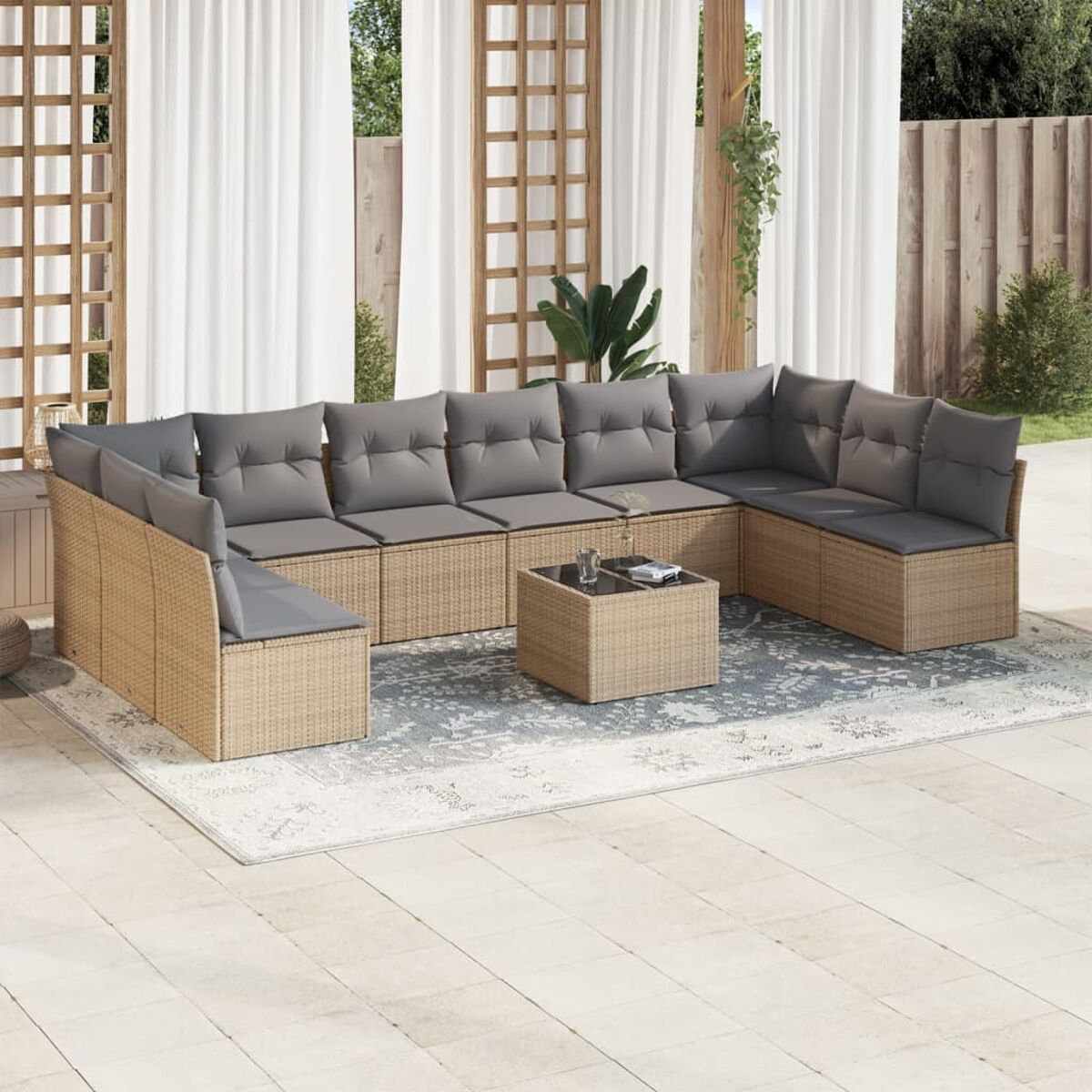 Beiges Wicker-Sofaset mit grauen Kissen auf einem Teppich. Ein Glastisch in der Mitte. Vorhänge und grüne Pflanzen im Hintergrund.