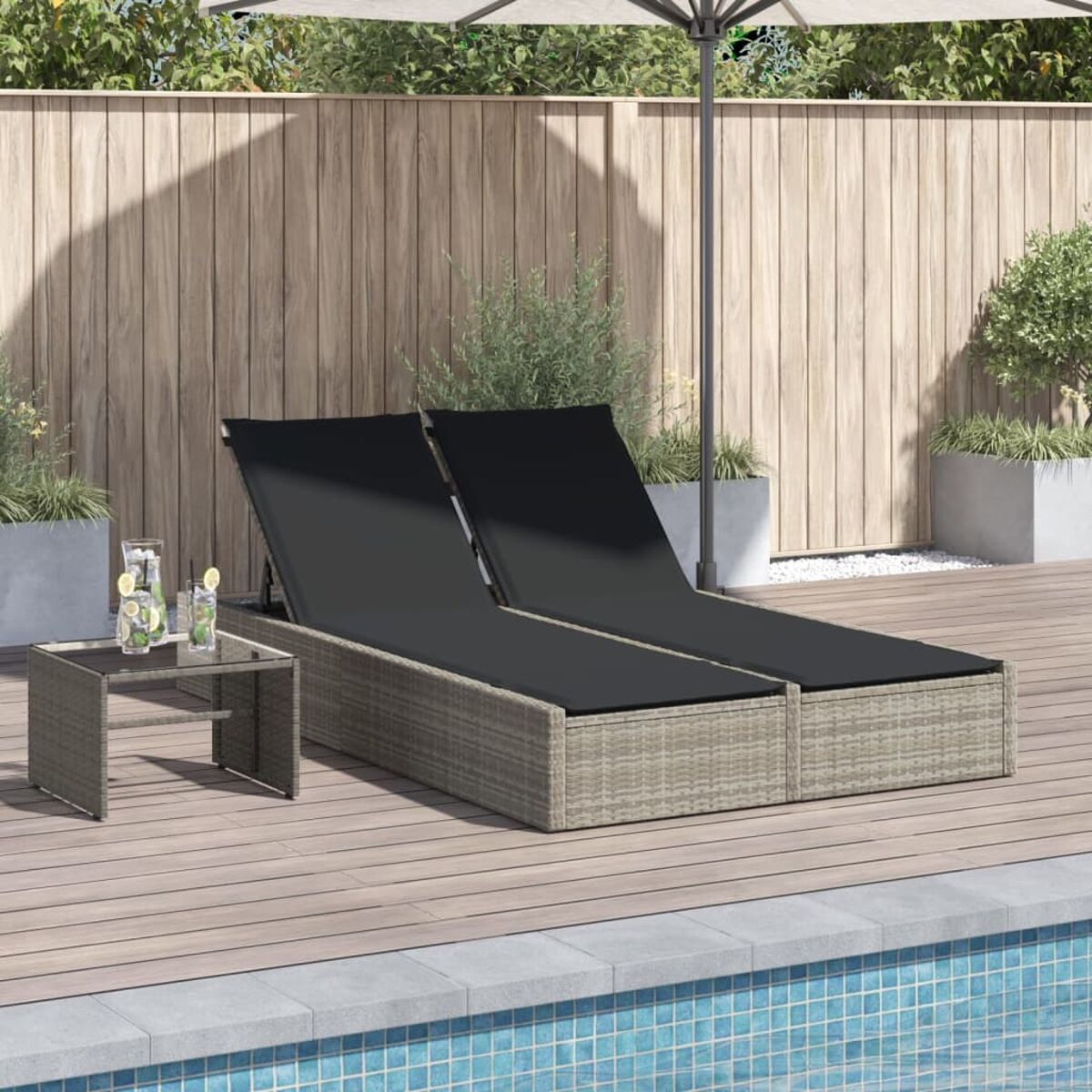 Zwei Outdoor-Liegestühle mit schwarzen Kissen an einem Pool. Ein kleiner Tisch mit Getränken.