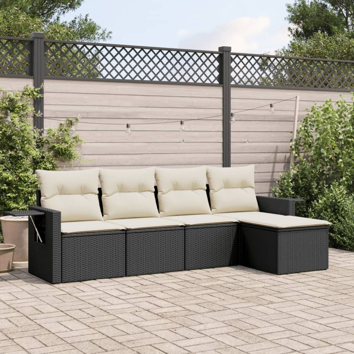 Schwarzes Outdoor-Sofa mit cremefarbenen Kissen auf einer Ziegelterrasse, in der Nähe von Pflanzen und Zaun.