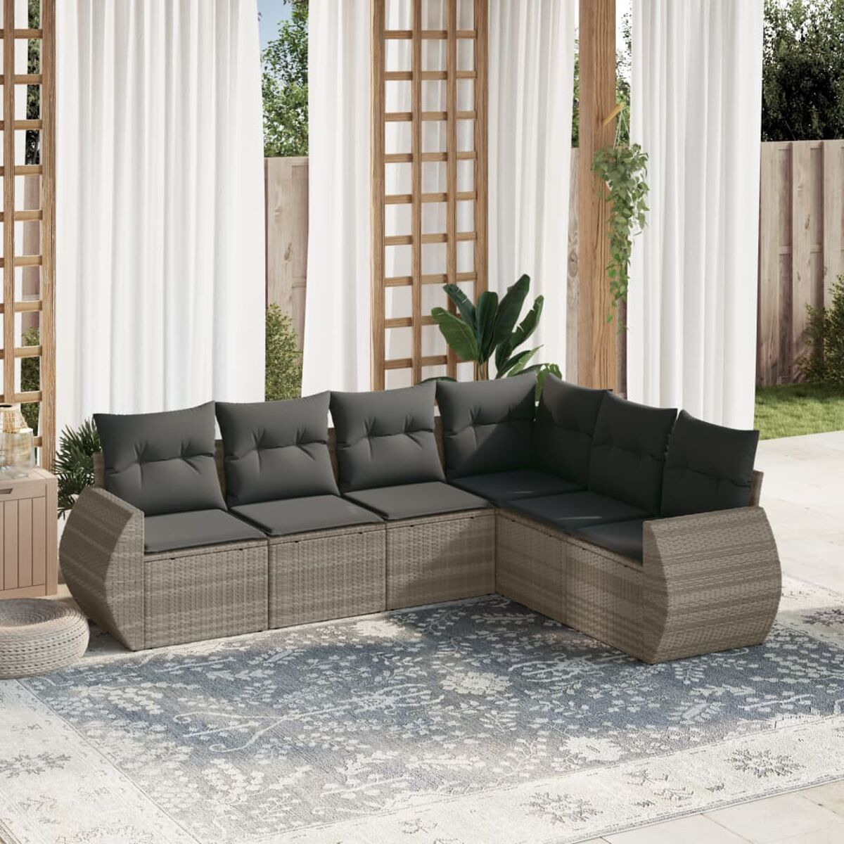 Beiges Outdoor-Ecksofa aus Korbgeflecht mit grauen Kissen auf blauem Musterteppich.