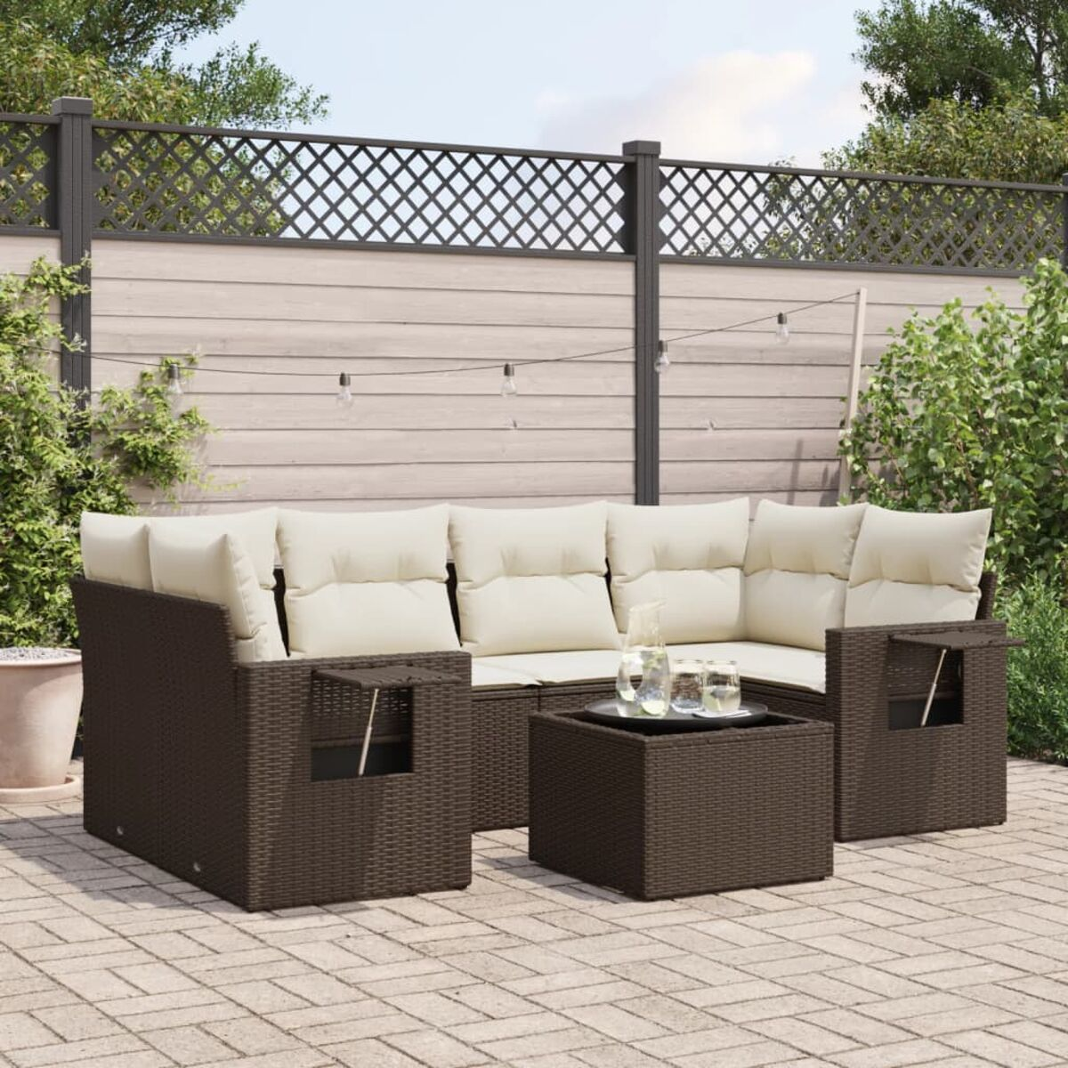 Divano componibile da esterno in rattan marrone scuro con cuscini color crema e tavolino quadrato, vista patio.