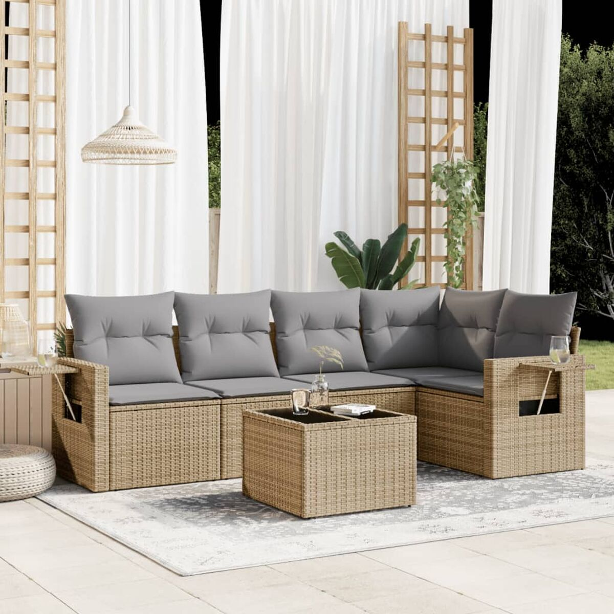Geflochtenes Ecksofa mit grauen Kissen und einem Couchtisch. Weiße Vorhänge und ein Teppich im Hintergrund.