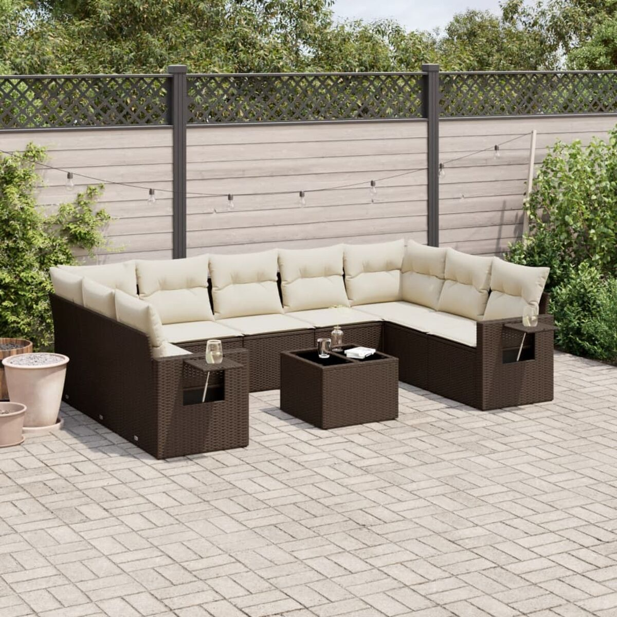 Dunkelbraunes Wicker-Sofaset mit cremefarbenen Kissen. Eine Backstein-Patio und ein Holzzaun im Hintergrund.