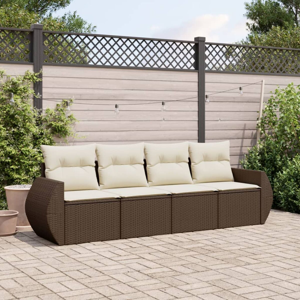 Divano in vimini marrone con cuscini beige, su un patio in mattoni, con piante.