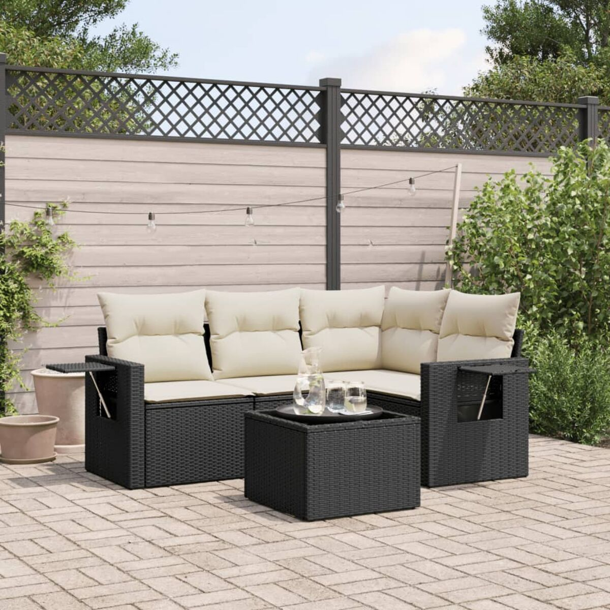 Schwarzes Rattan-Outdoor-Sofa mit cremefarbenen Kissen und Glastisch auf einer Ziegelterrasse.