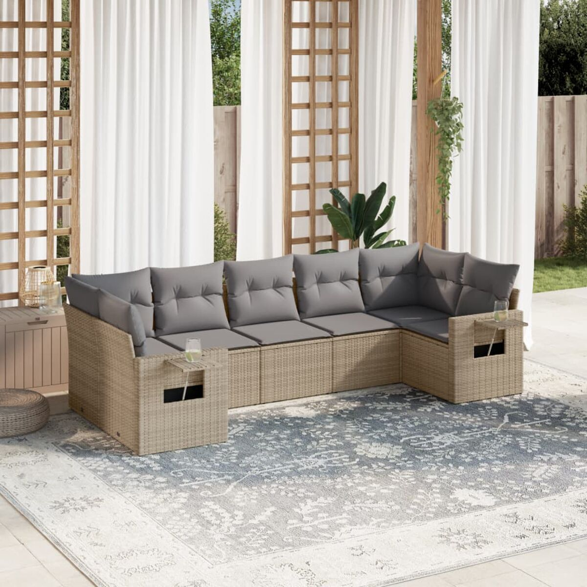 Ein Outdoor-Rattansofa mit grauen Kissen auf einem gemusterten Teppich, Vorhänge im Hintergrund.