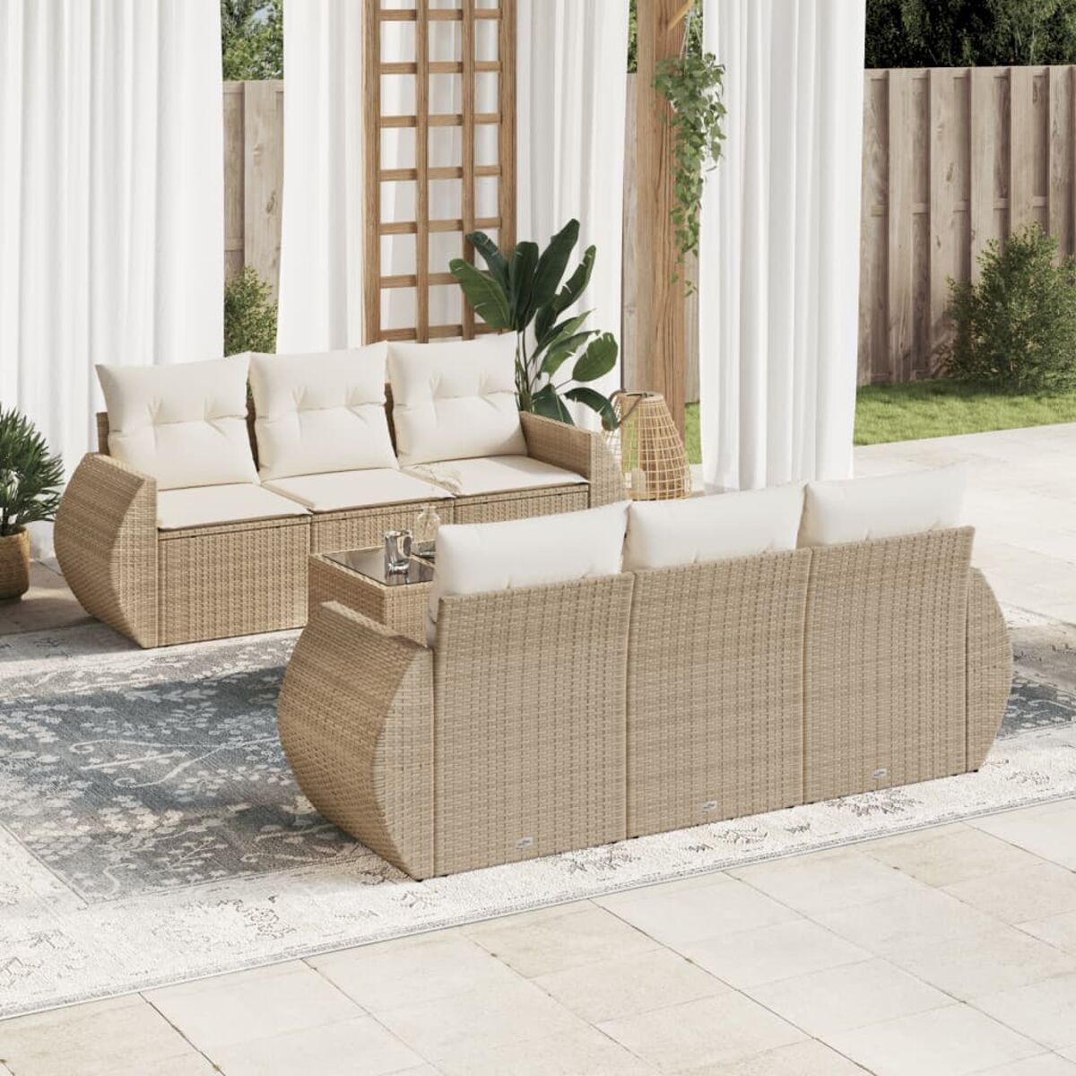 Zwei Sets aus Outdoor-Sofas aus Korbgeflecht mit weißen Kissen und einem kleinen Glastisch auf einer Terrasse.